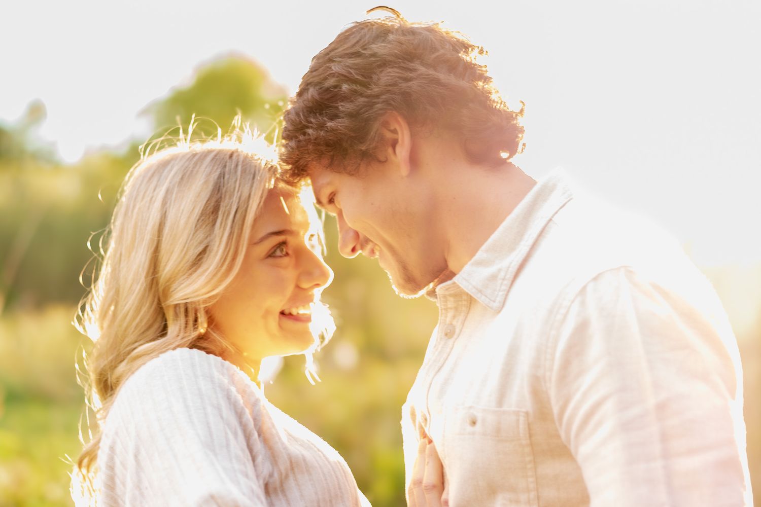 A romantic couple shares an intimate moment in a sunlit field during golden hour.