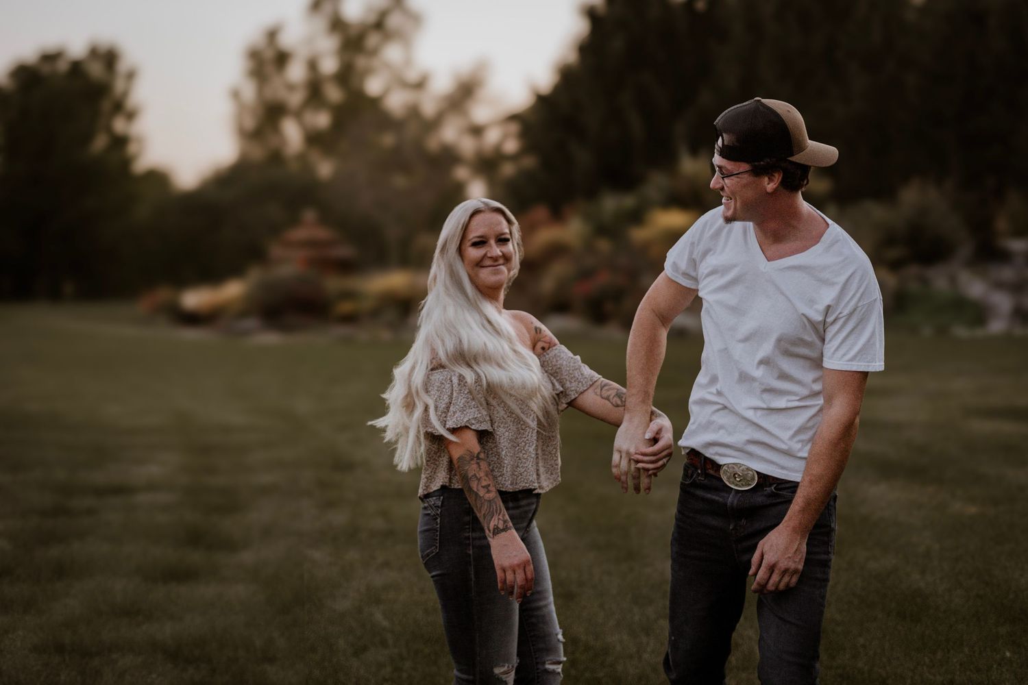 Couple in casual wear sharing playful moment in grassy field during golden hour.