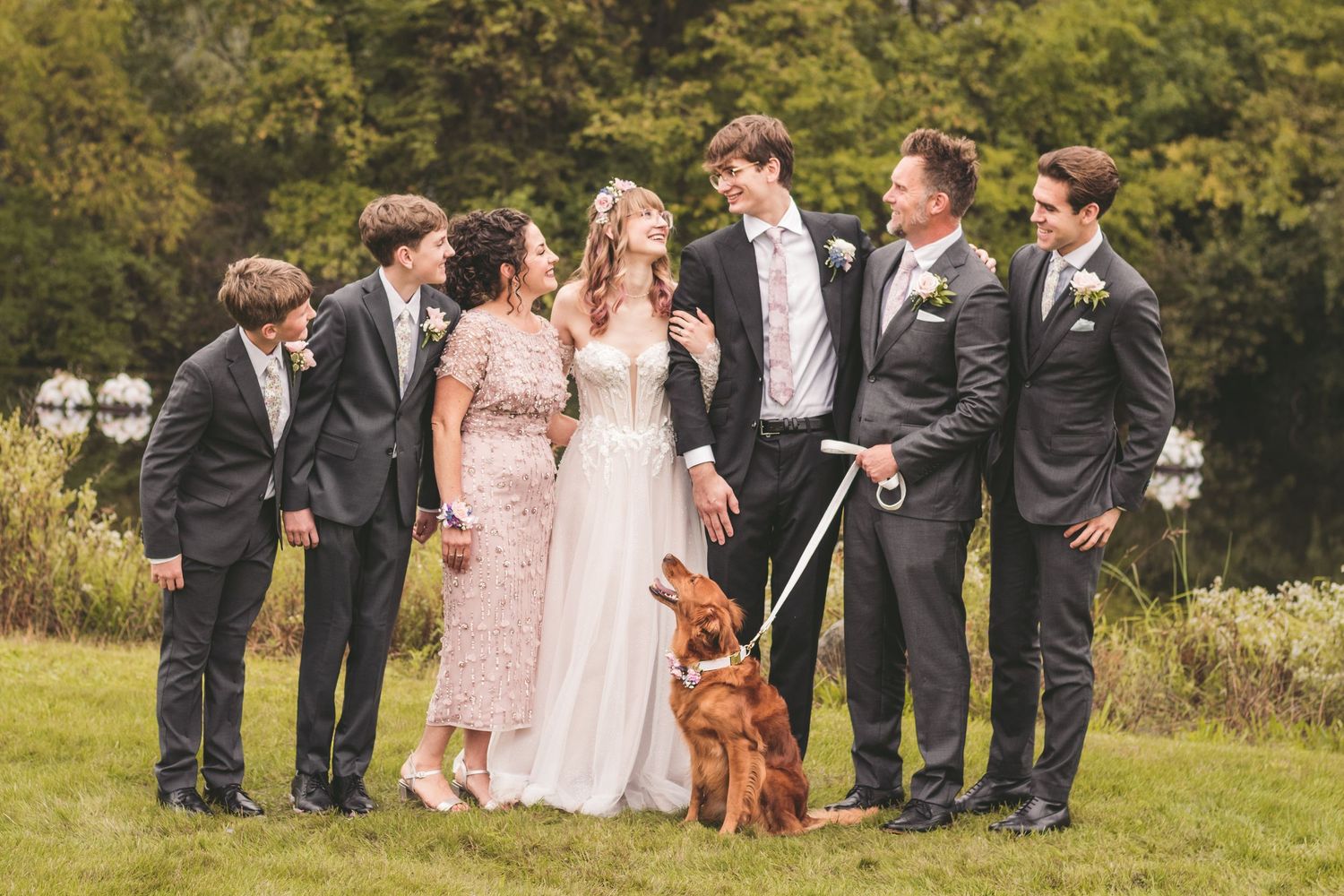Wedding party group with bride, groom, family members, and a red Irish Setter dog outdoors.