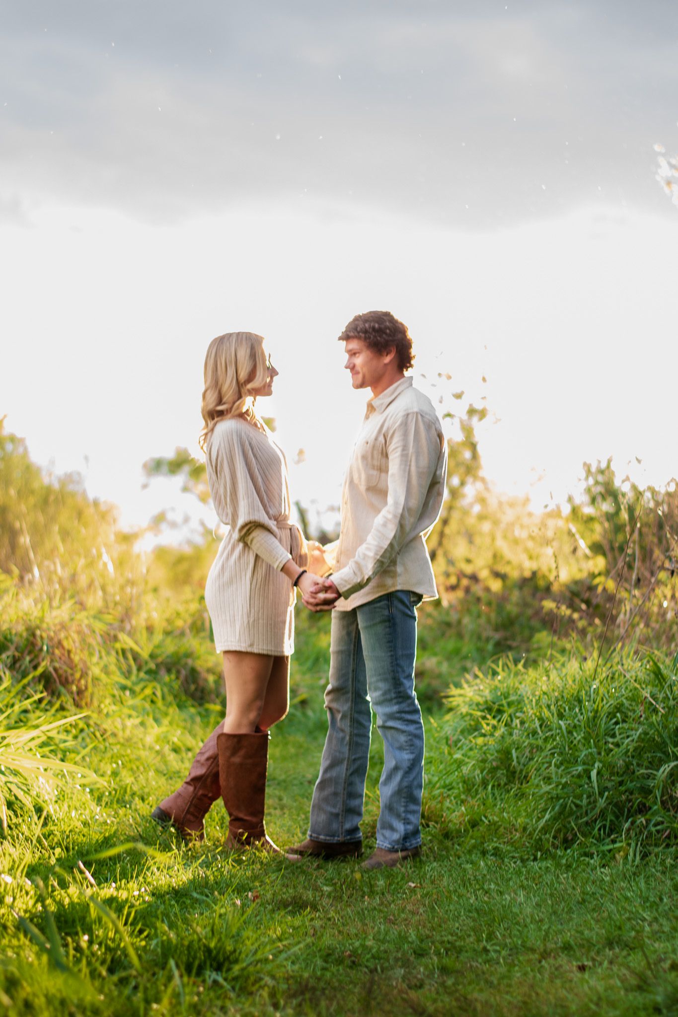 A couple stands together on a grassy hilltop during golden hour.