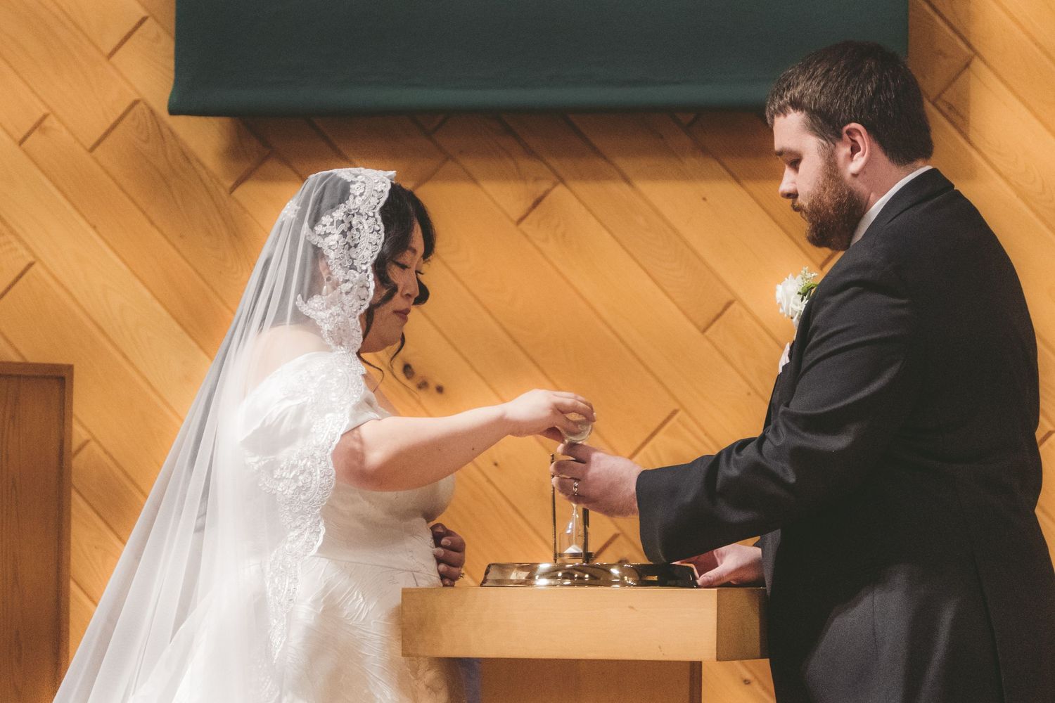 Bride and groom exchanging rings at the altar during a wedding ceremony in a wood-paneled church.