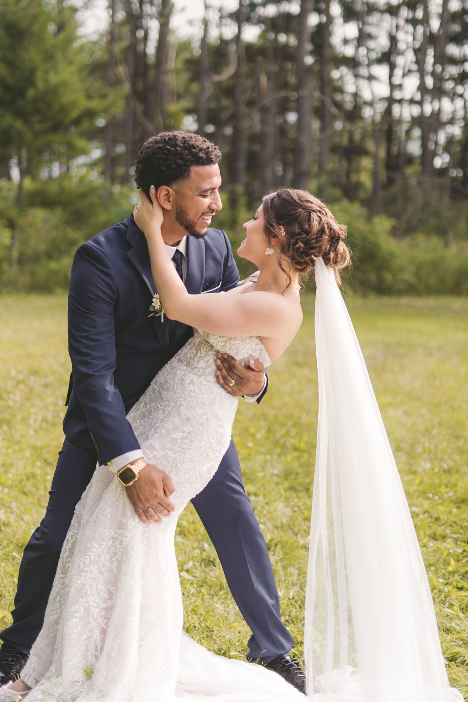 Bride and groom share a romantic dance outdoors, with the bride in a lace gown and veil, groom in a navy suit.