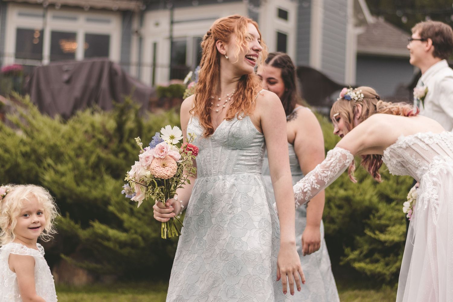 Joyful redhead bridesmaid in blue lace dress holding bouquet laughing outdoors at wedding celebration.