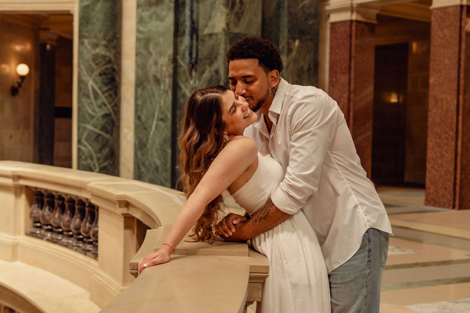 Romantic couple sharing a kiss on an elegant marble balcony in a luxurious indoor venue.