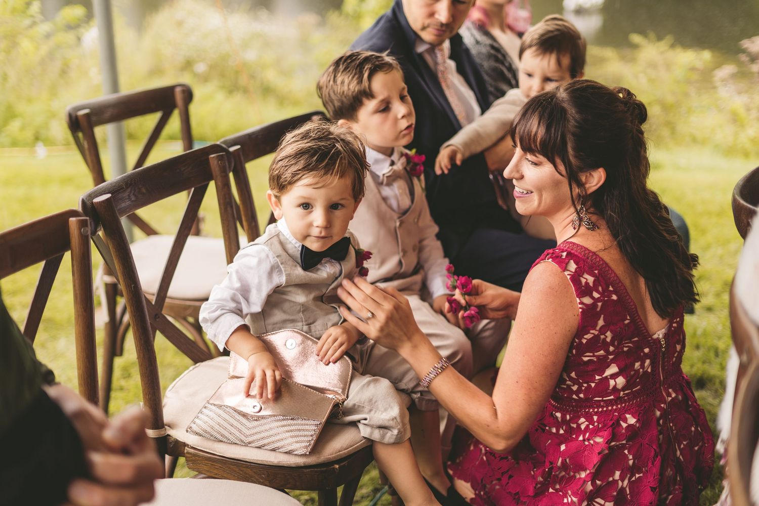 Woman in red sequin dress interacts with young boys in suits at an outdoor wedding ceremony.