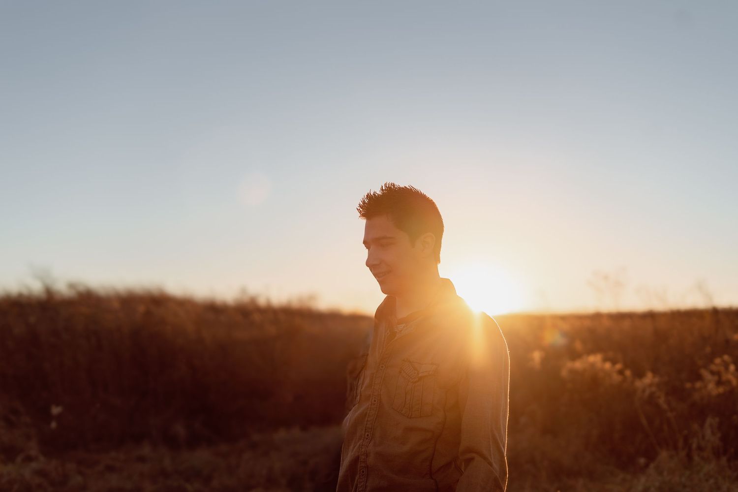 Silhouette of a person standing in a golden sunset field with warm backlight and clear sky.