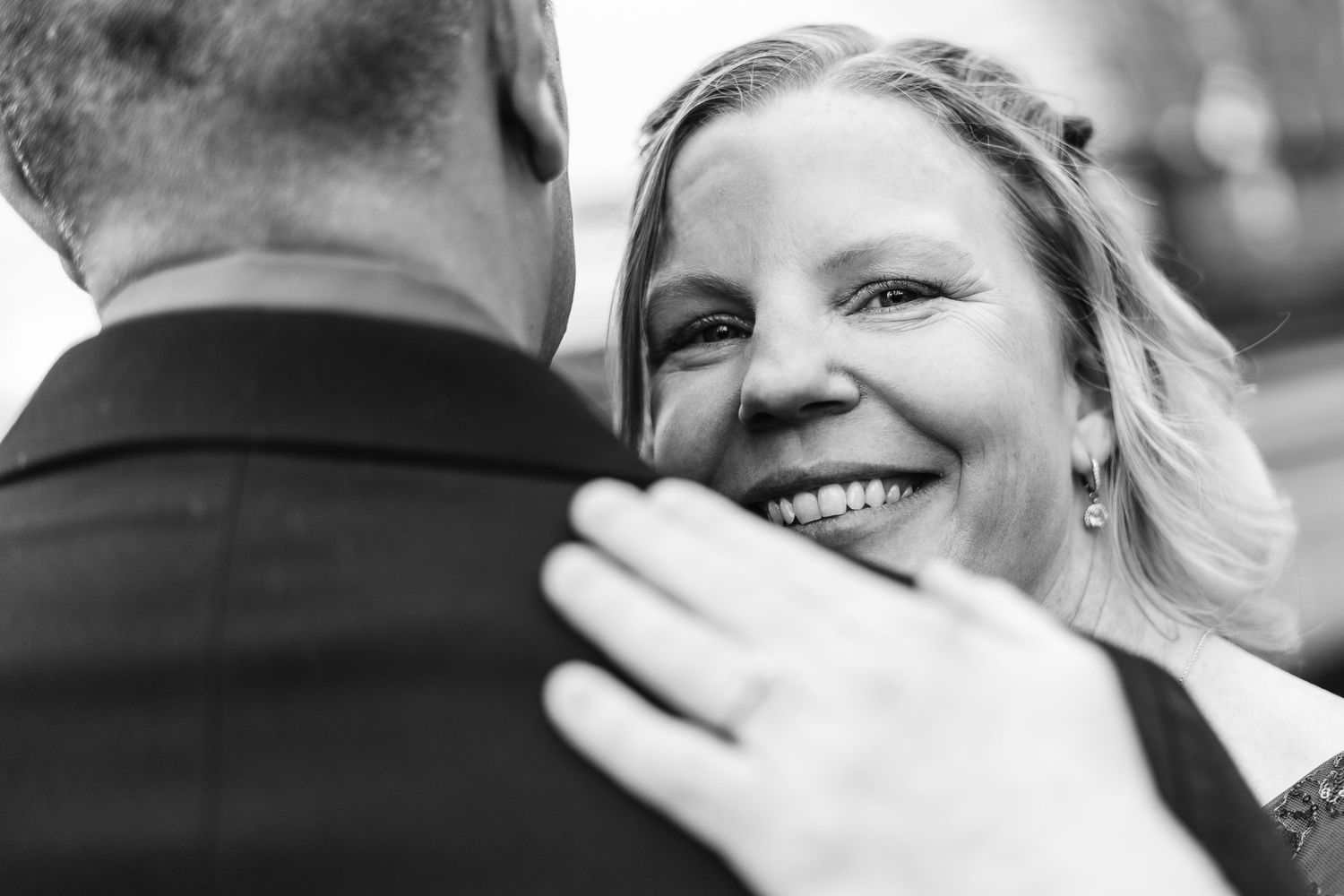Black and white photo of a smiling bride embracing her groom at a wedding ceremony.