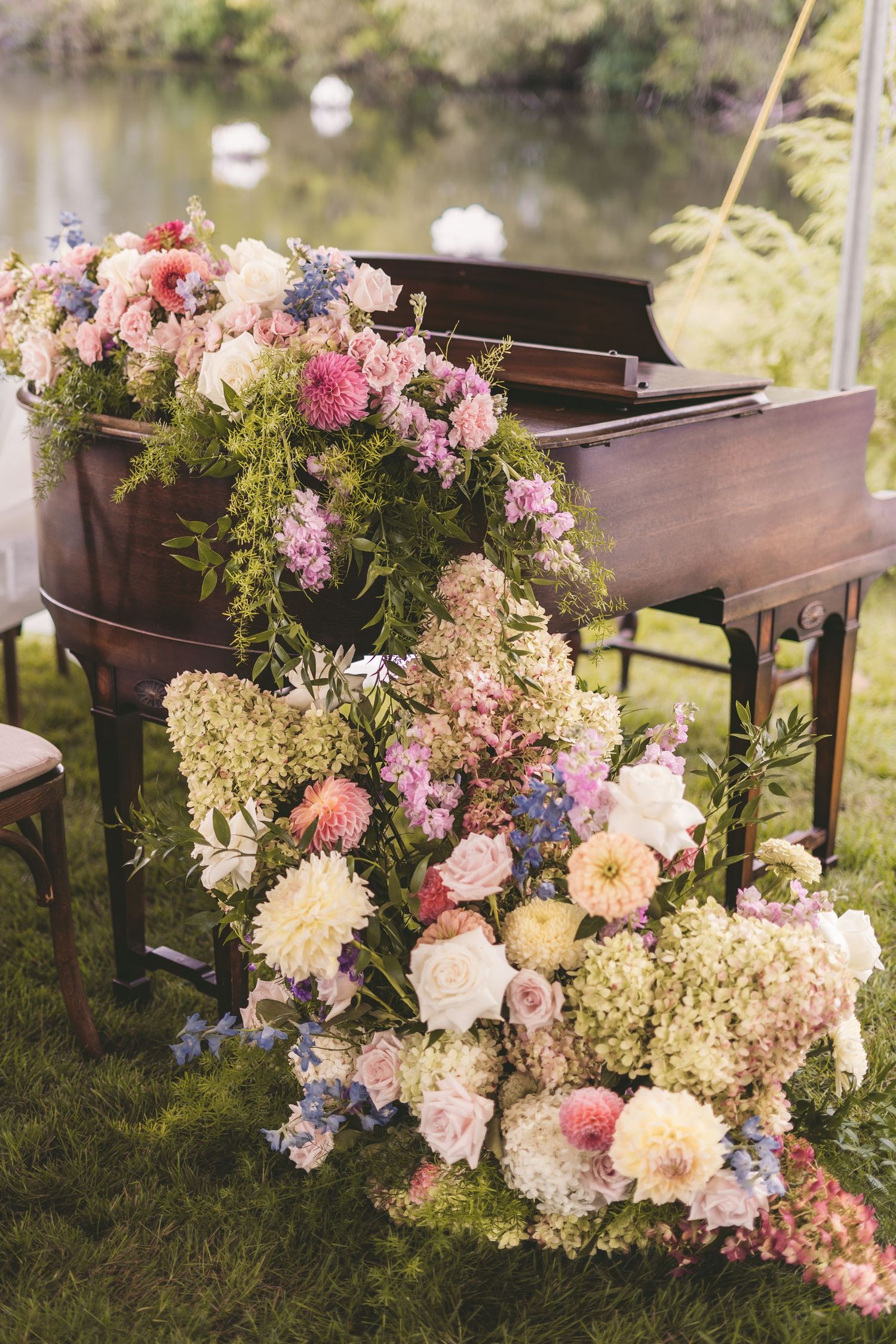 Elegant grand piano adorned with lush cascading floral arrangement of pink dahlias, hydrangeas, and greenery outdoors.