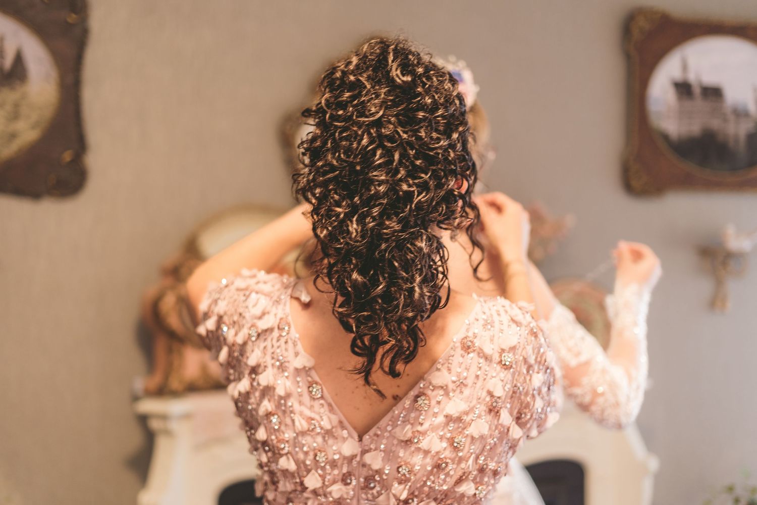 Bride with curly brown hair in lace wedding dress seen from behind.