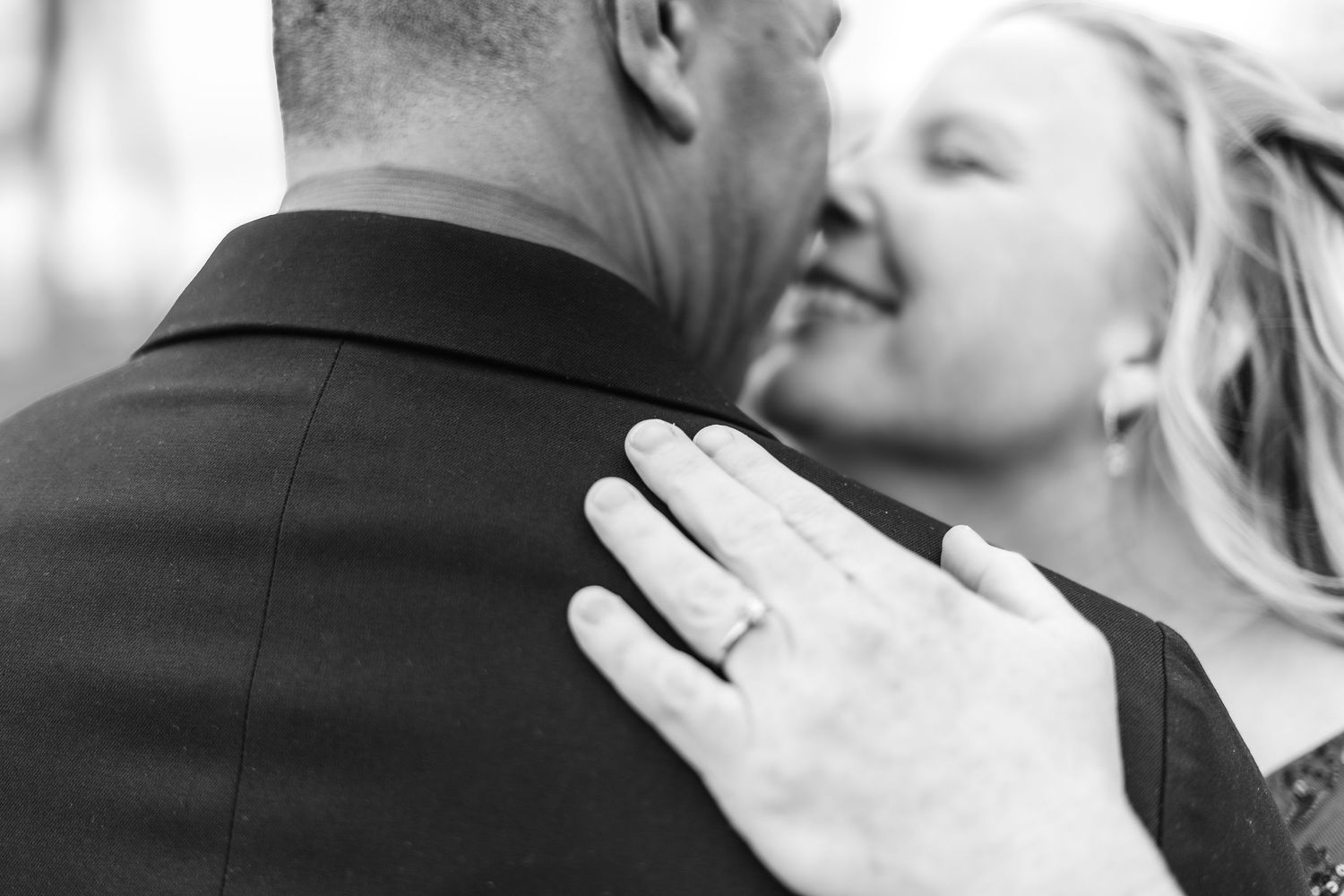 Black and white photo of a couple embracing, showcasing an engagement ring on the woman's hand.