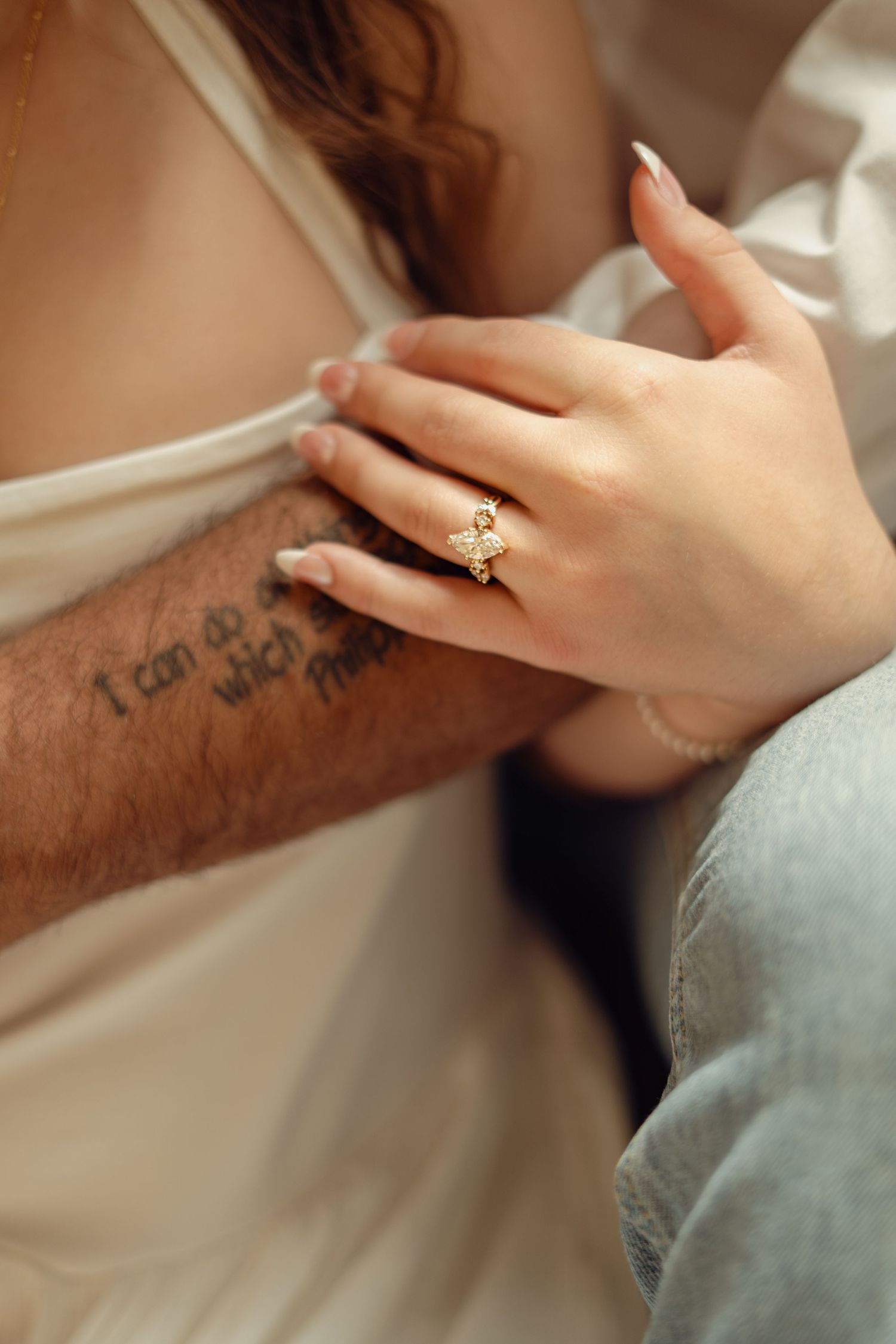 Close-up of a woman's hand with a gold diamond engagement ring resting on a man's tattooed arm.