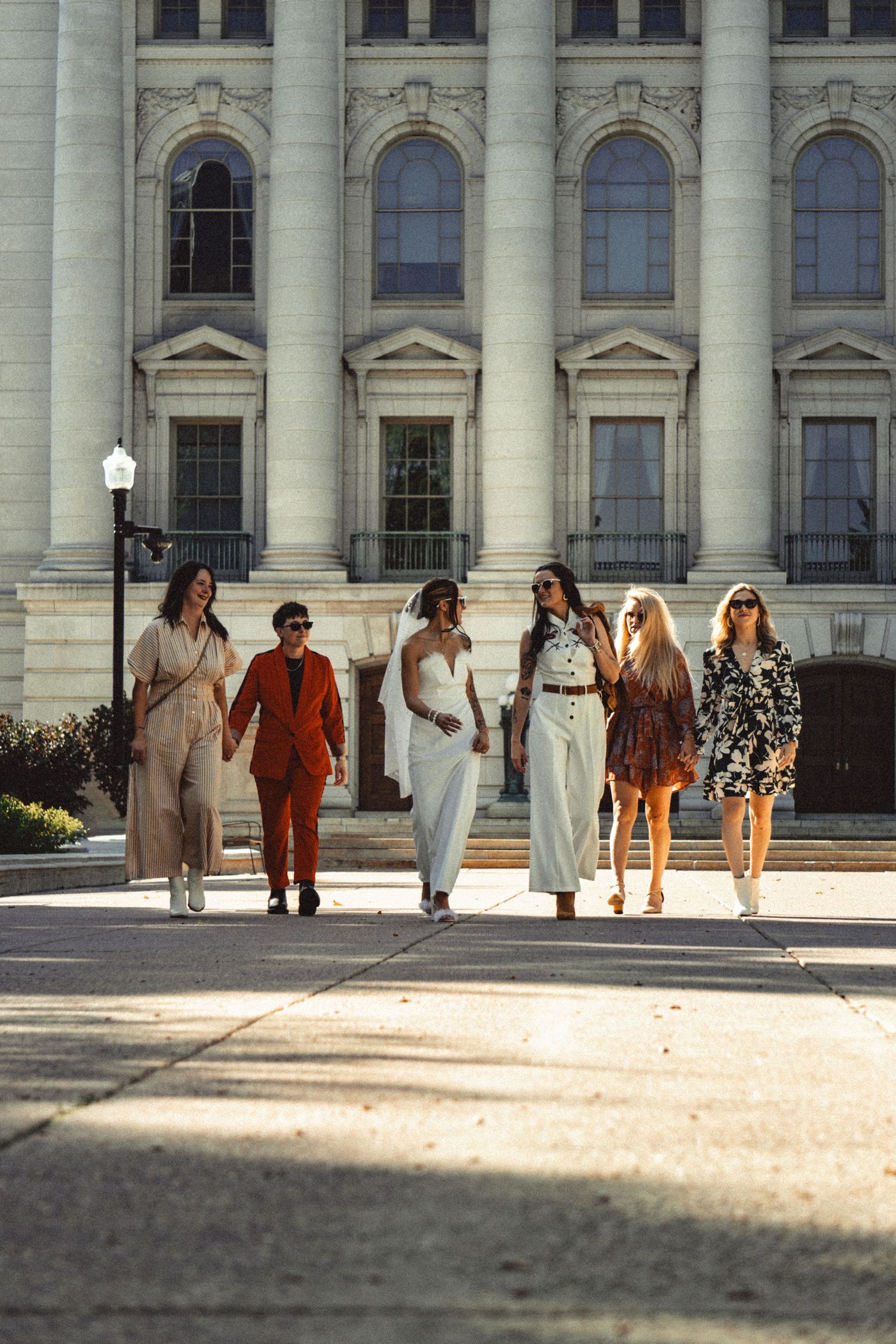 Bride and group walking in front of ornate building with columns on sunny day.