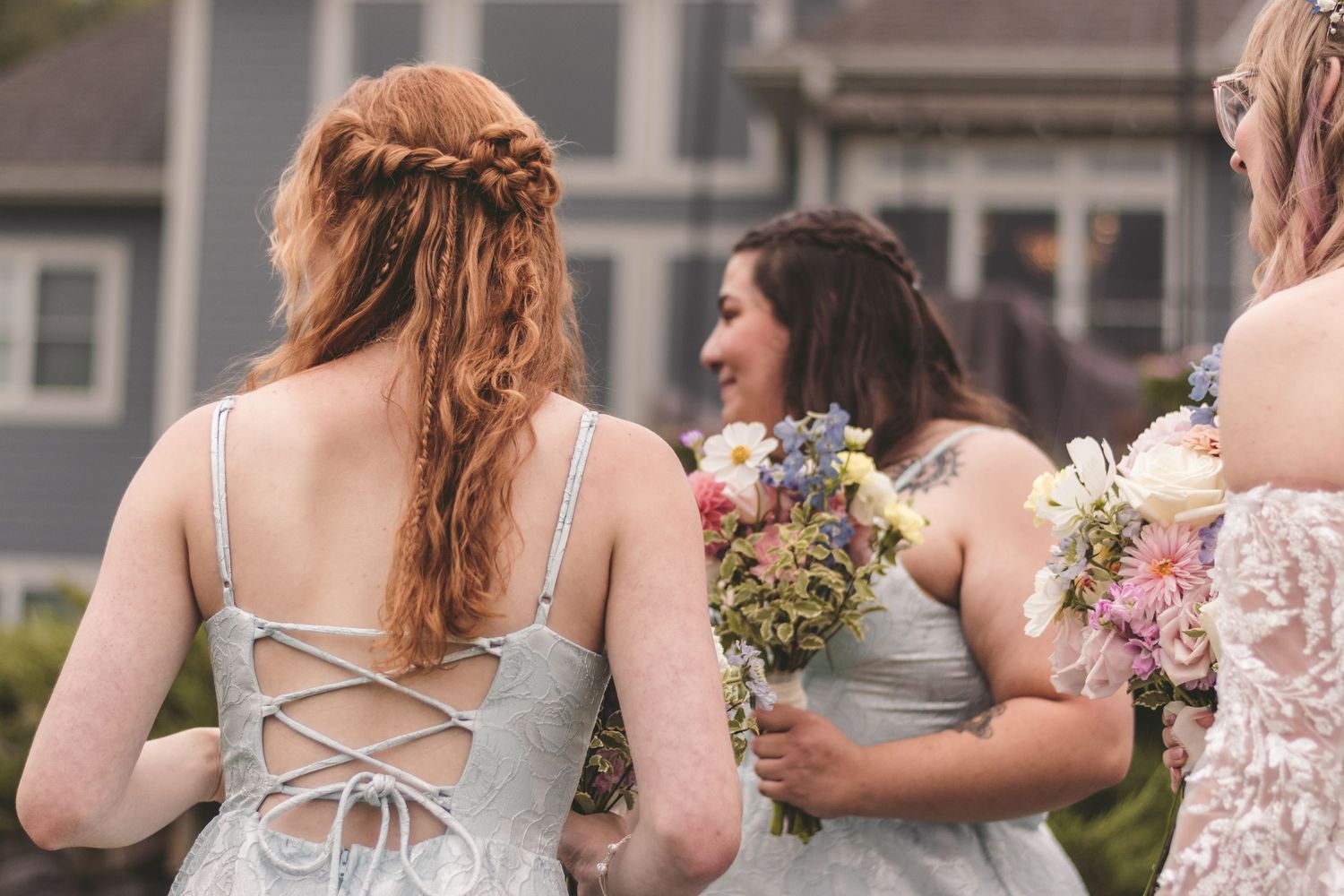 Bridesmaids in silver lace-up dresses holding wildflower bouquets walking together outdoors.