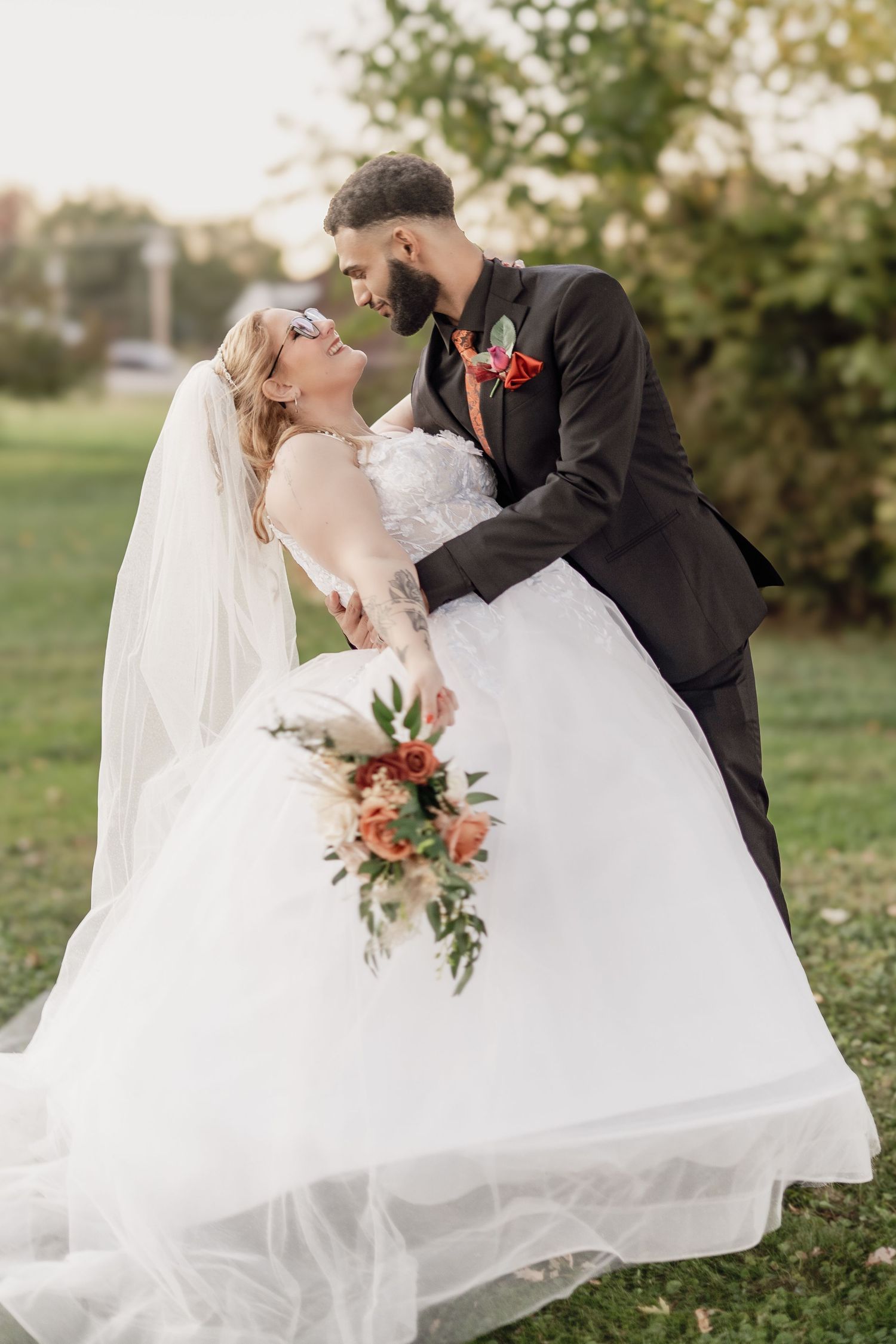 A romantic wedding photo shows a couple in formal attire sharing an intimate moment outdoors with a fall-colored bouquet.