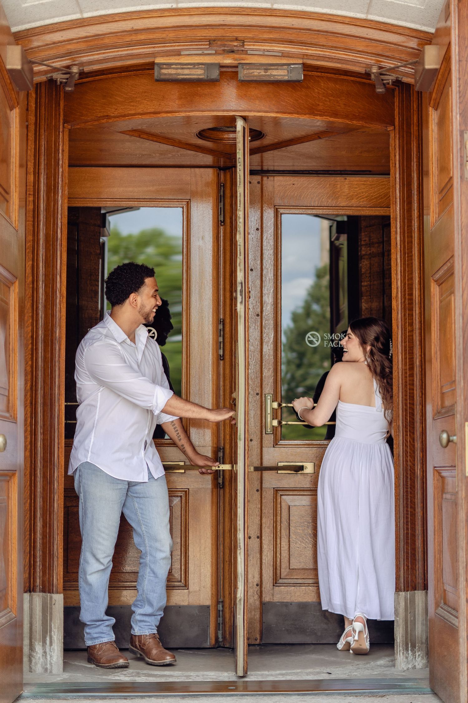 Interracial couple entering through ornate wooden double doors of a historic building.