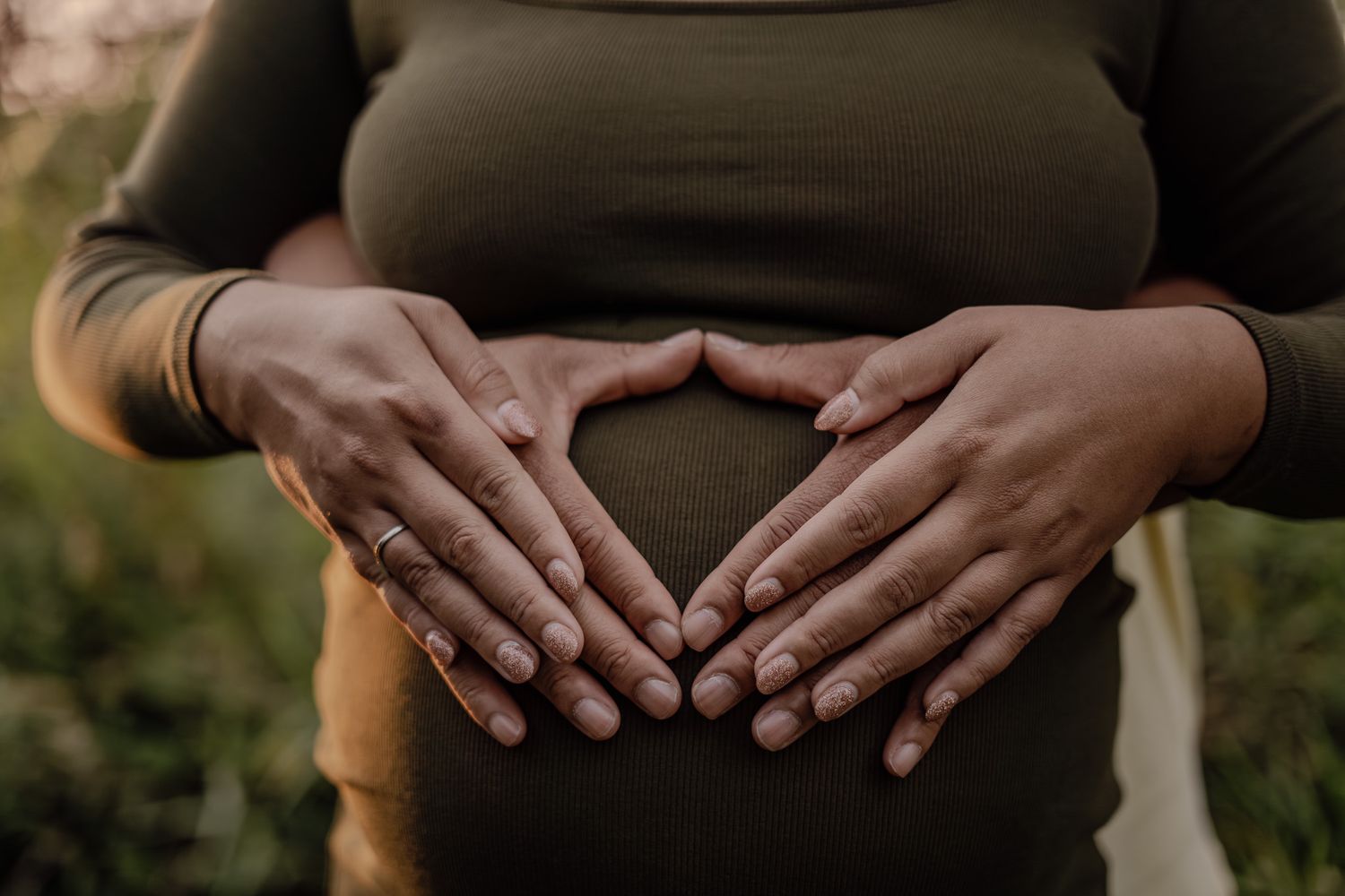 Close up of hands forming a heart shape over a pregnant belly.