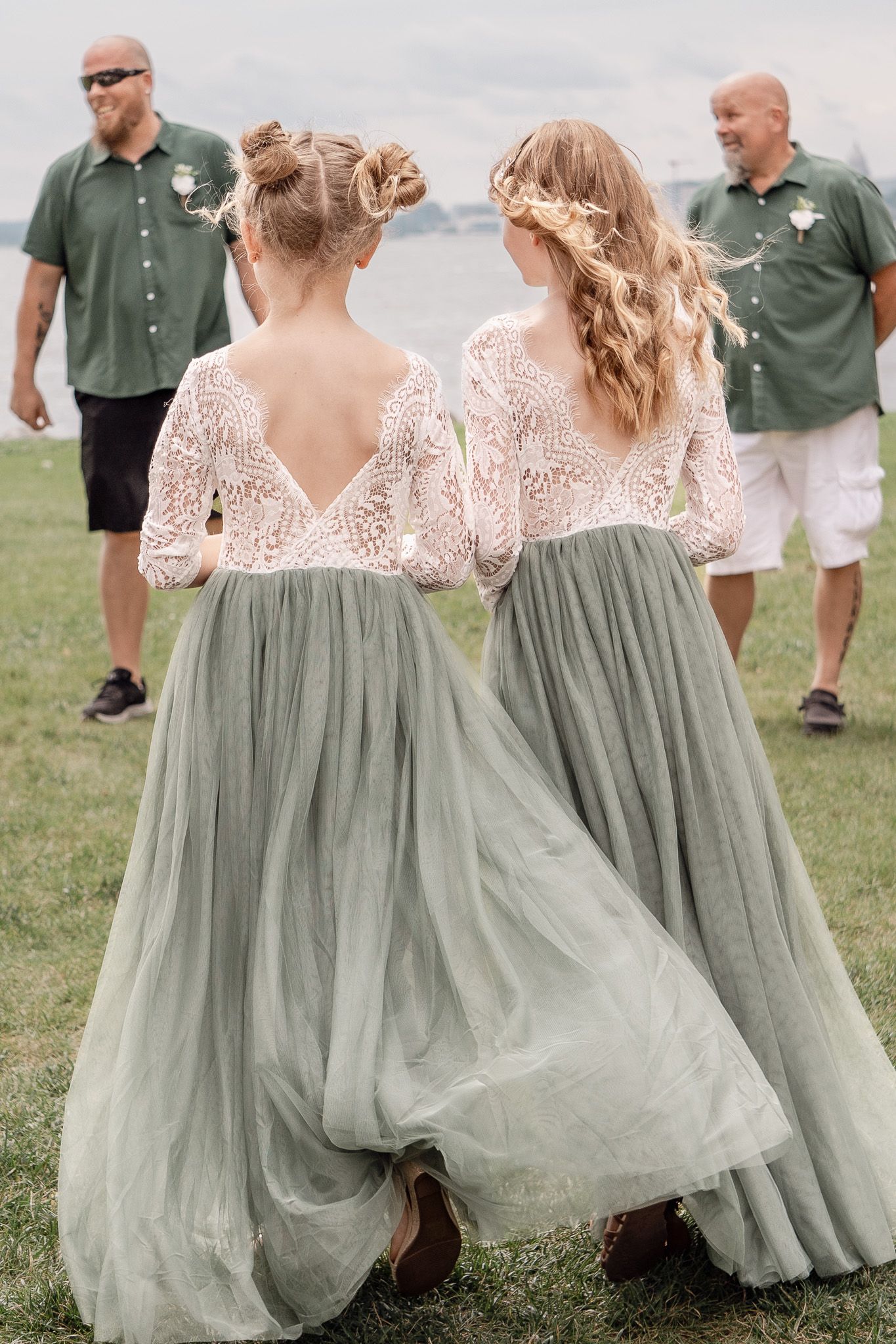 Two people in matching sage green dresses walk across a field.