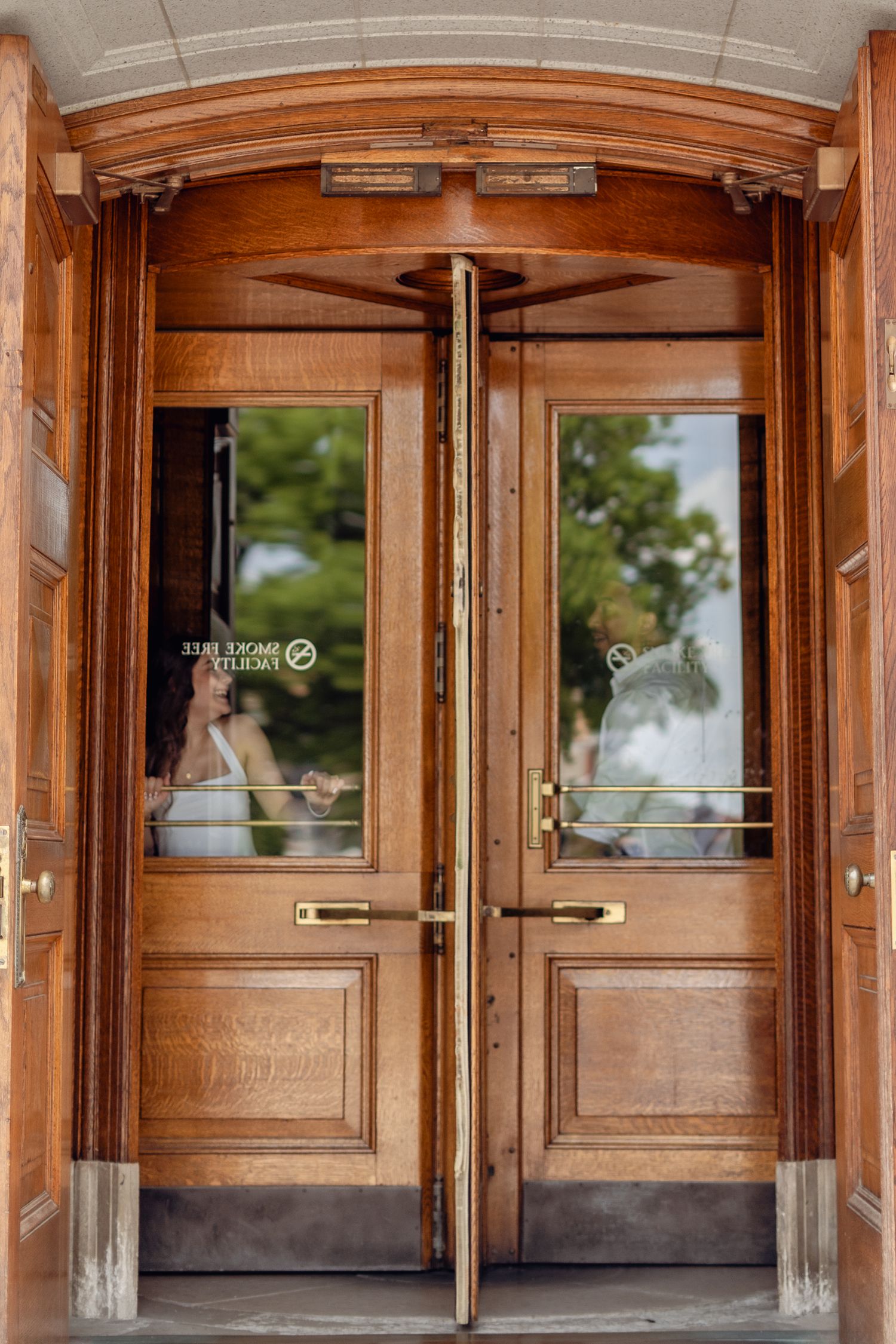 Elegant wooden double doors with brass handles and glass panels, featuring a classic arched entryway of a historic building.
