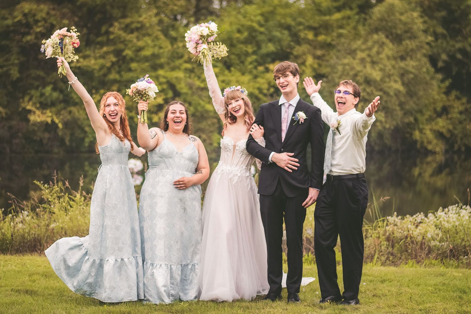 Joyful wedding party of bride, groom, and bridesmaids celebrating outdoors in a lush green garden setting.