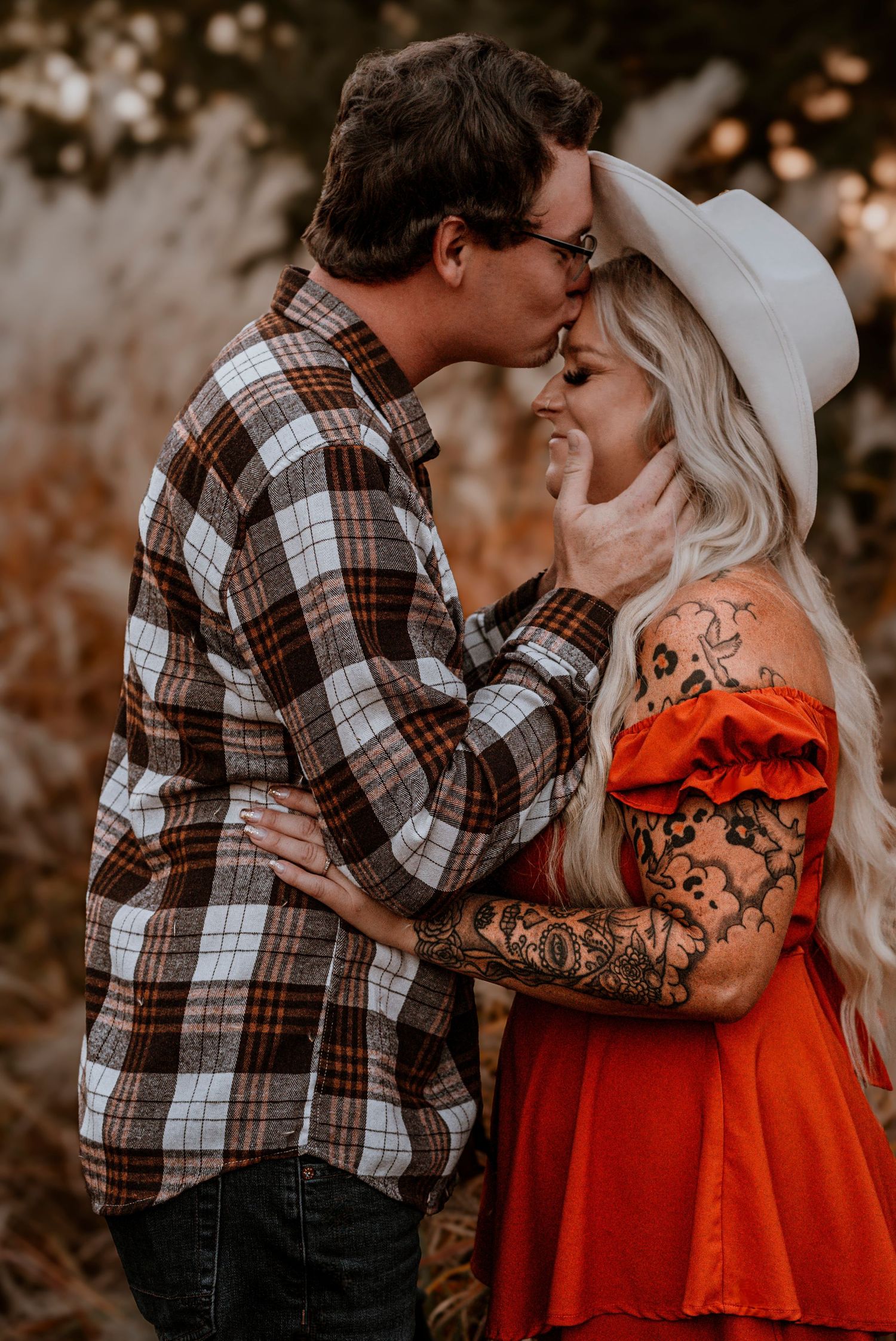 Romantic autumn couple embraces in plaid shirt and red dress with tattoo sleeve against blurred nature background.