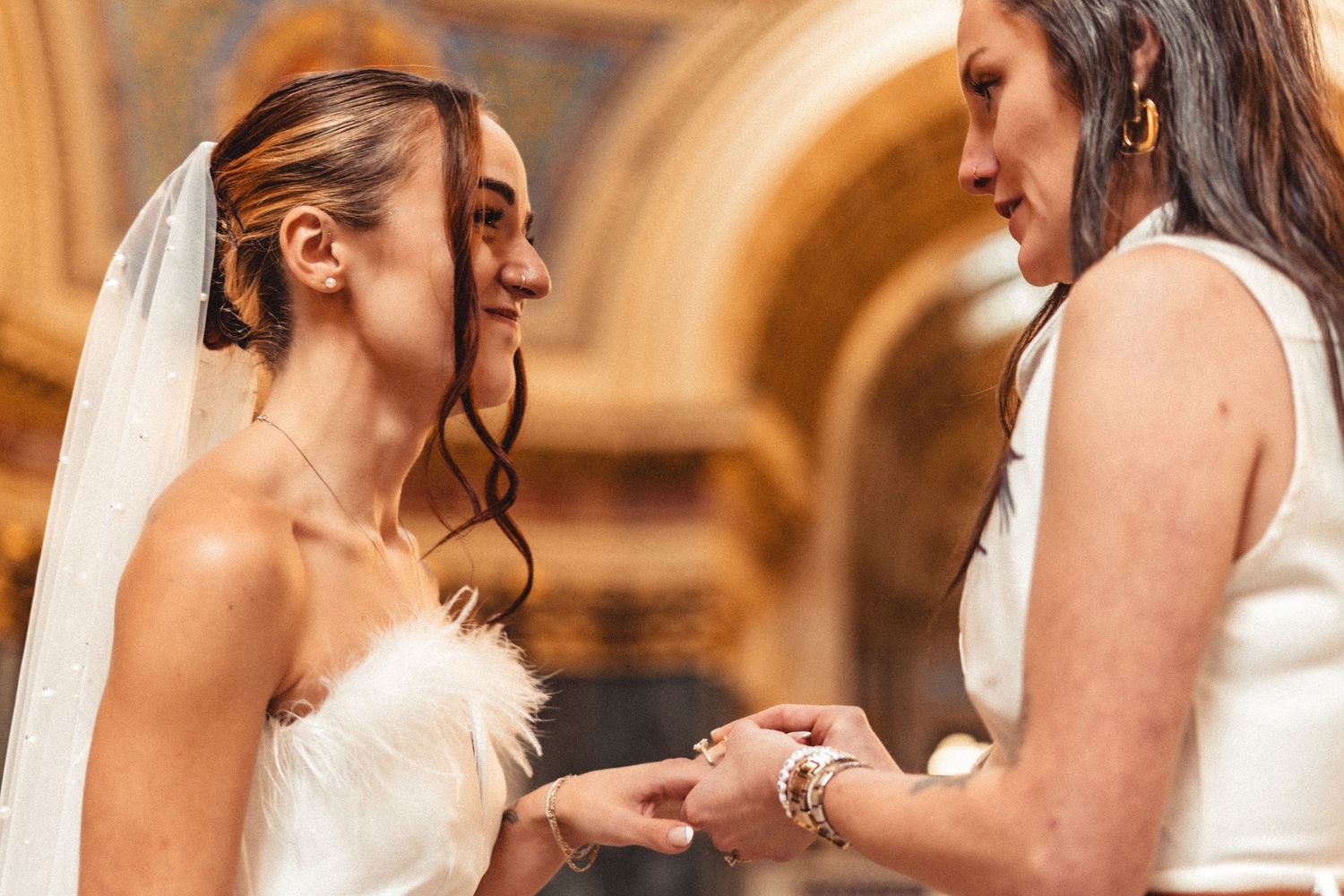 Bride and bridesmaids in elegant white dresses laugh together during a candid wedding moment.