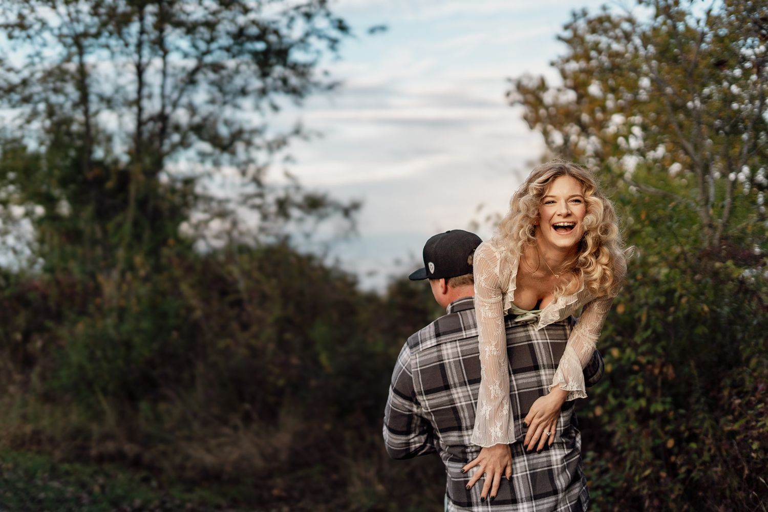 A romantic outdoor photoshoot in a natural setting with tall grass and cloudy skies at sunset.