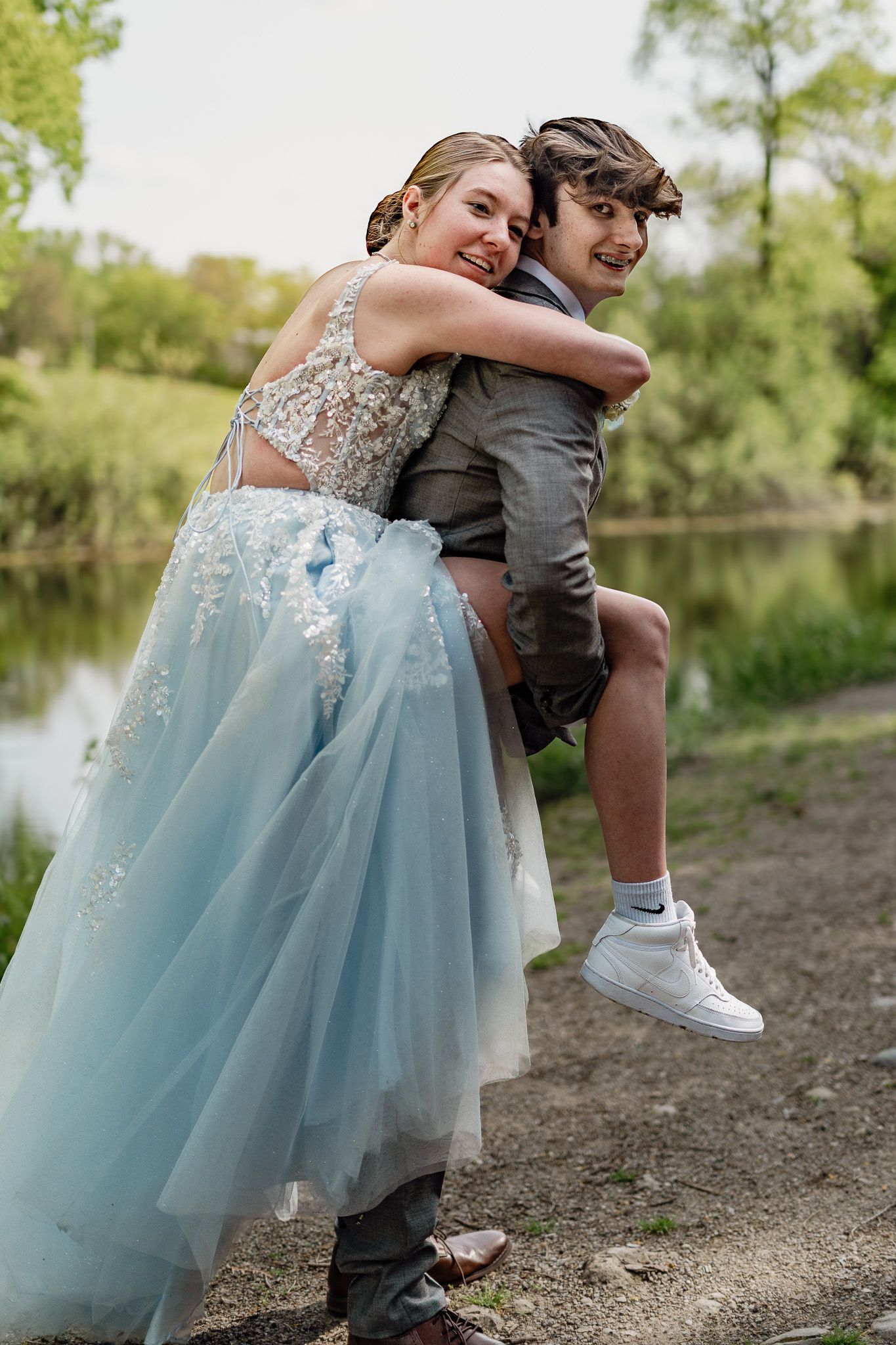 A playful prom photo with a couple in formal wear by a lake.