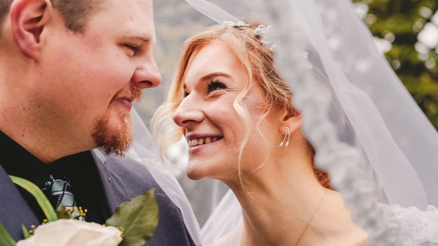 Romantic wedding couple moment captured through flowing white veil outdoors.