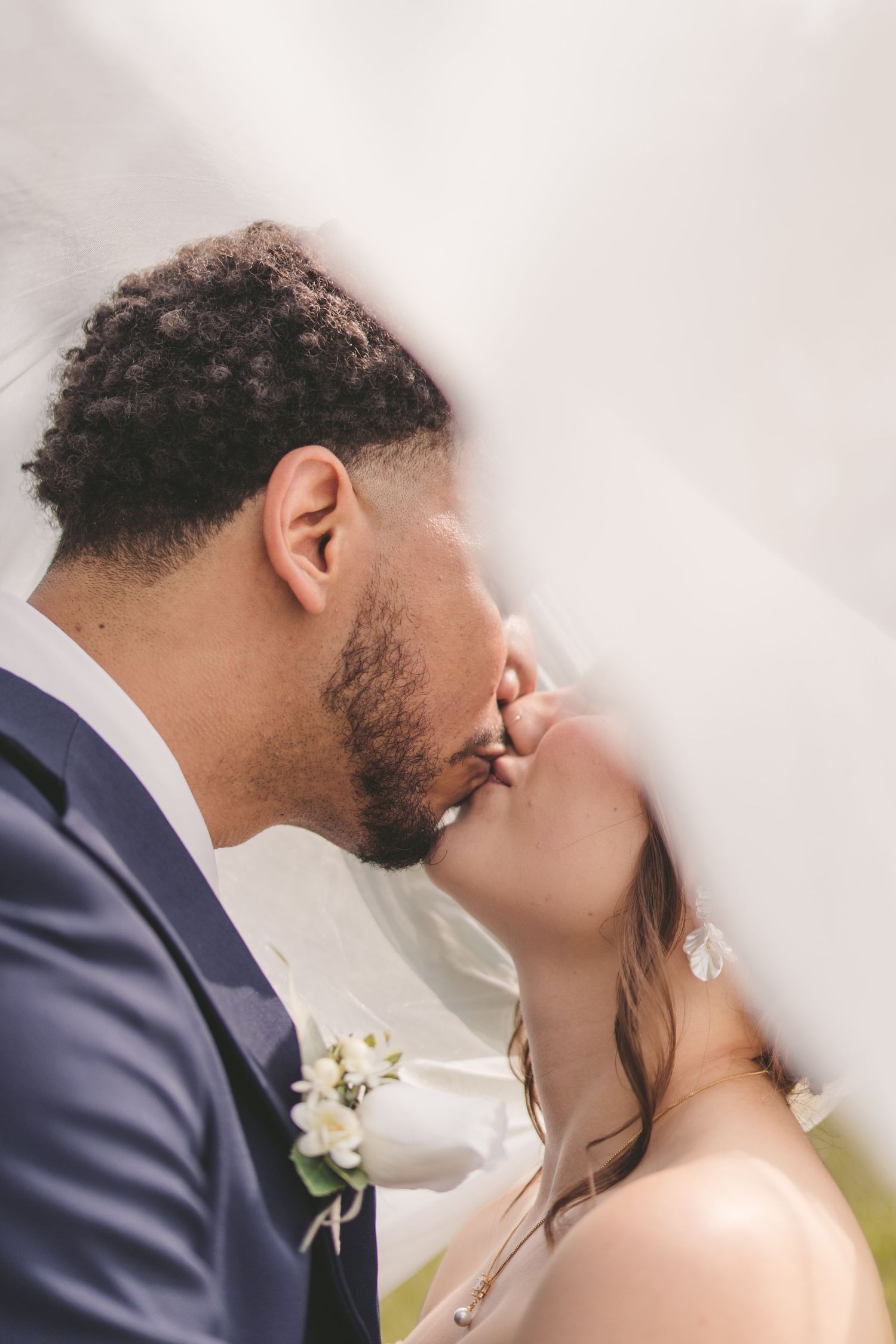 A bride and groom share a romantic kiss under a flowing white veil on their wedding day.