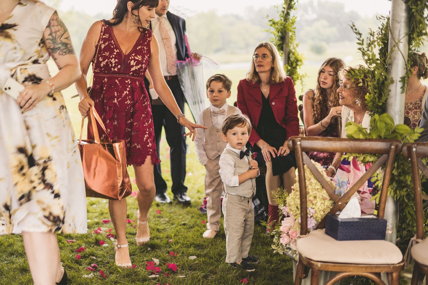 Wedding guests walking on grass with young boy in suspenders among the crowd.