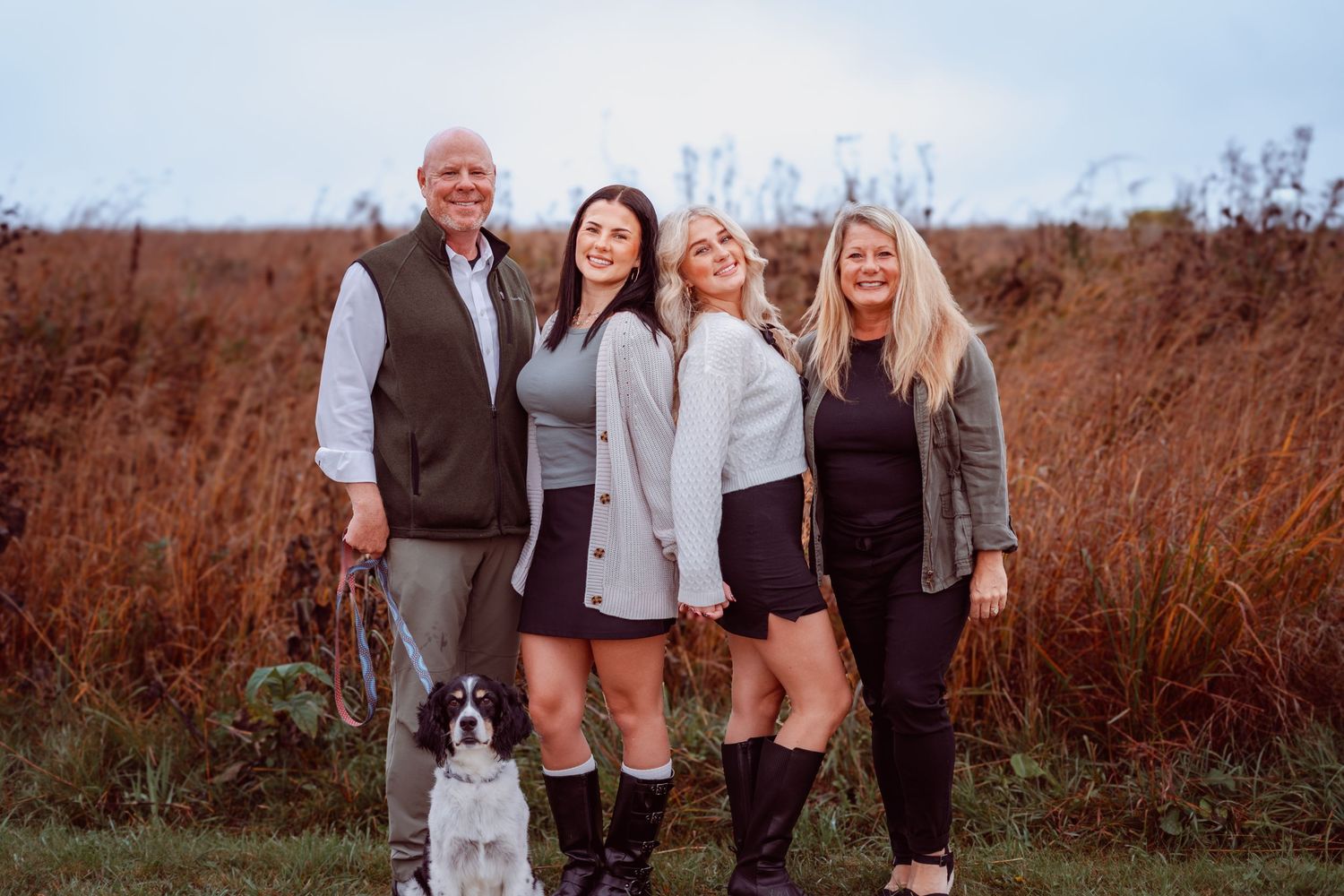 Family portrait with dog and adult children in autumn field with tall grass background.