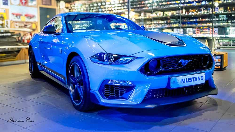 Blauwe Ford Mustang gefotografeerd op een tentoonstelling, automotive fotografie met dramatische belichting en een stedelijke achtergrond.