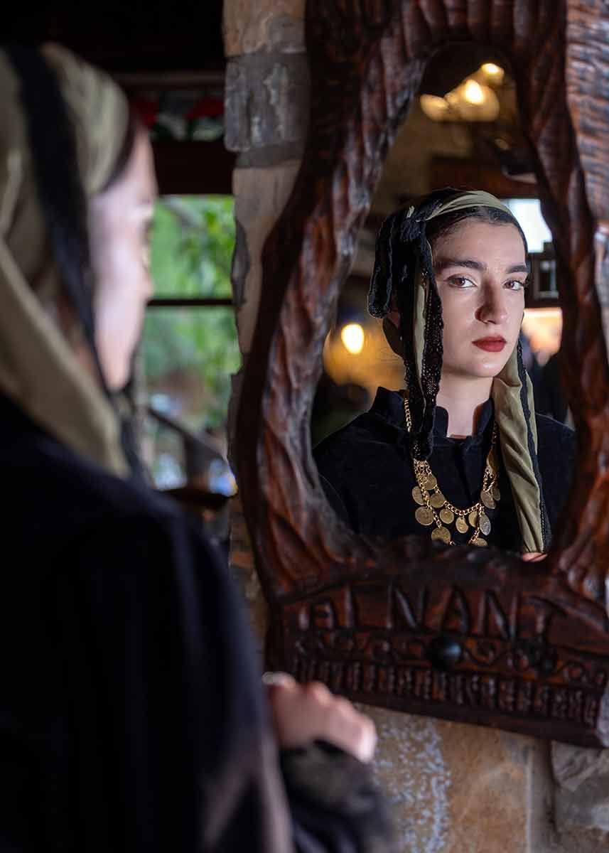Redactioneel portret van een vrouw in traditionele kleding, weerspiegeld in een antieke spiegel.