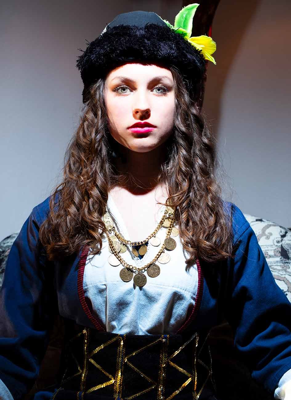 Kleurportret van een vrouw in traditionele klederdracht en sieraden tegen een neutrale achtergrond.
