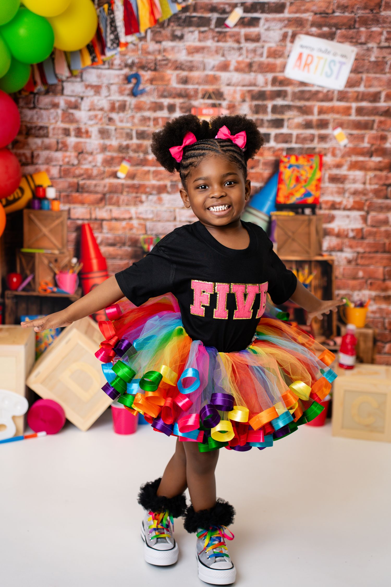 A young girl in a rainbow tutu and black FIVE shirt poses for her 5th birthday party photo.