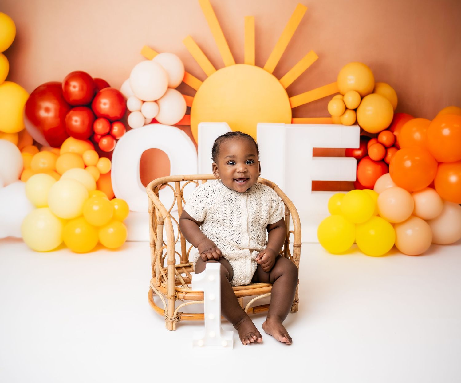 Metro Detroit children photographer Orange and yellow balloon decorations create a sunny backdrop for a cake smash photo session.