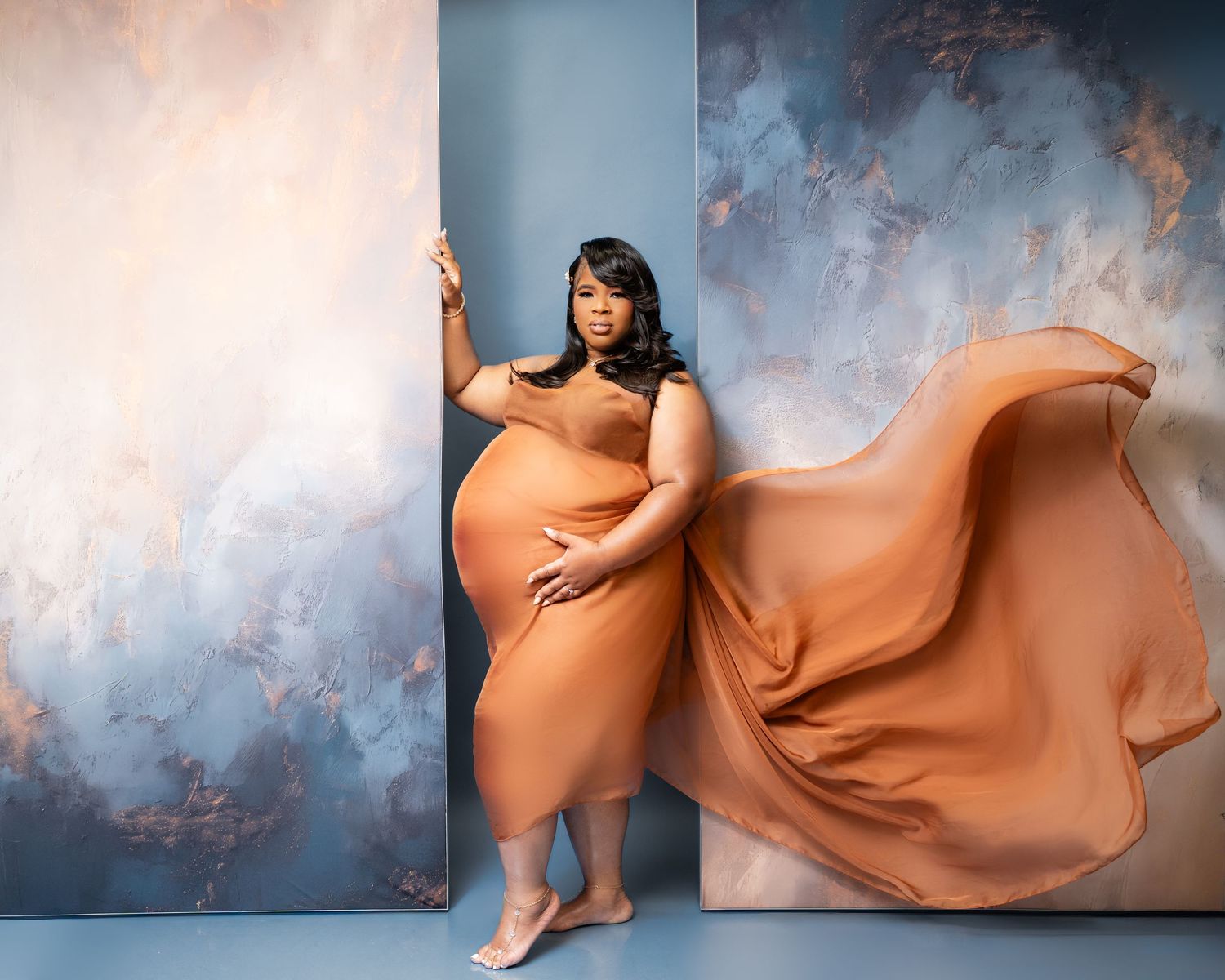 Metro Detroit maternity photographer capturing an expecting mom maternity portrait with billowing orange fabric against painted backdrop.