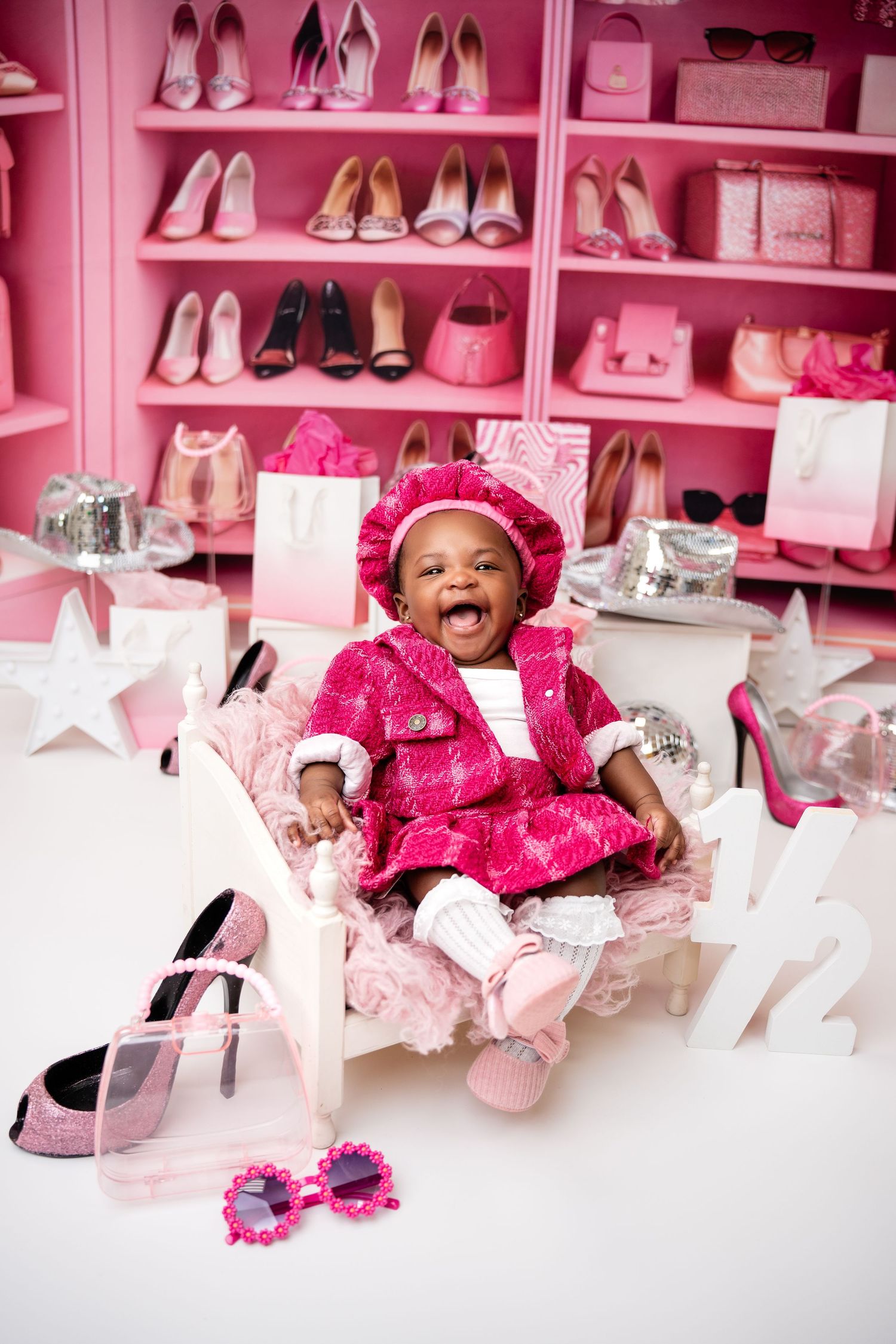 Pink themed photo shoot with baby surrounded by shoes and feminine accessories.
