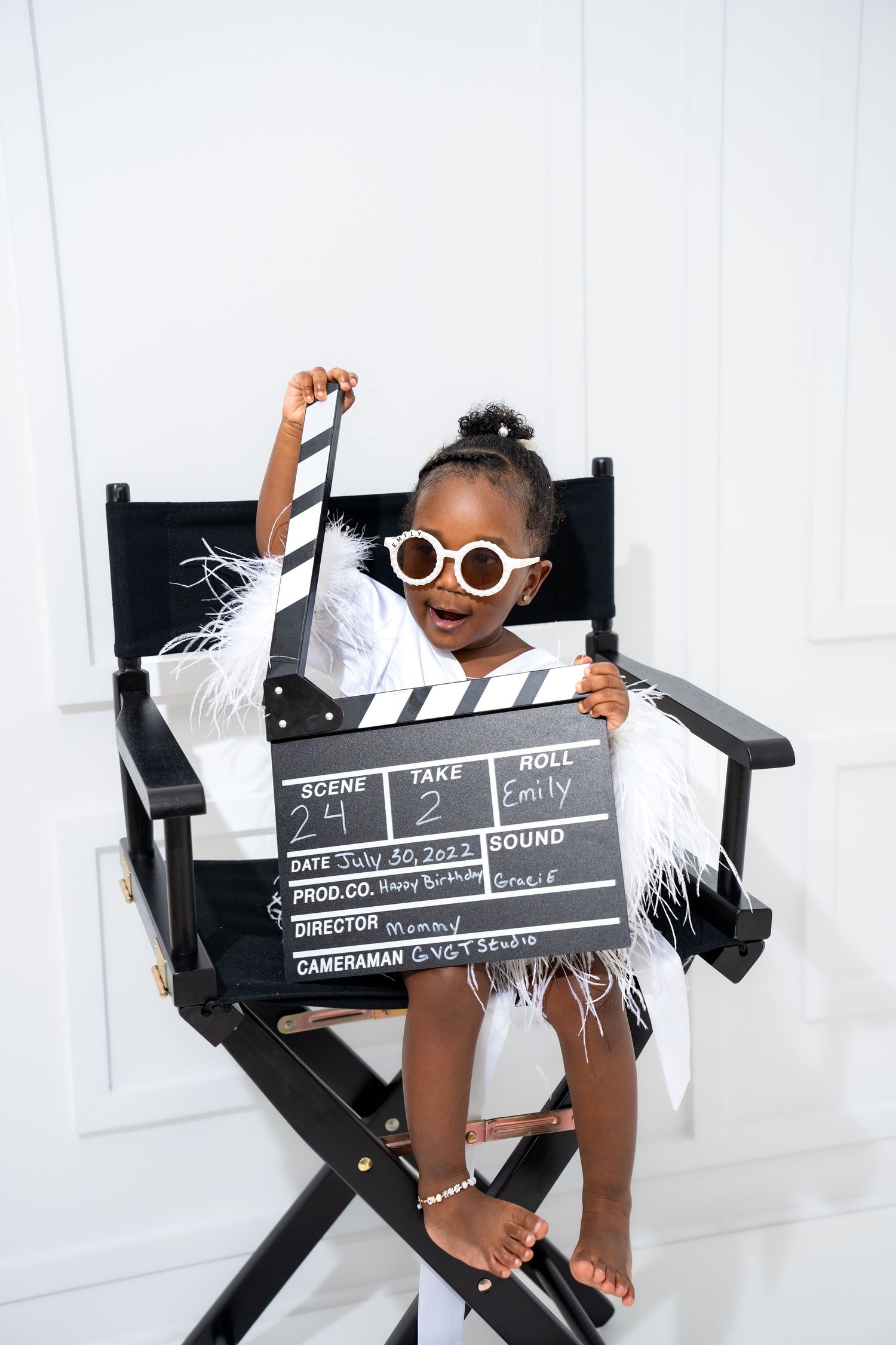 Metro Detroit children photographer photographing a toddler in Movie-themed photo shoot with director's clapperboard and black chair.