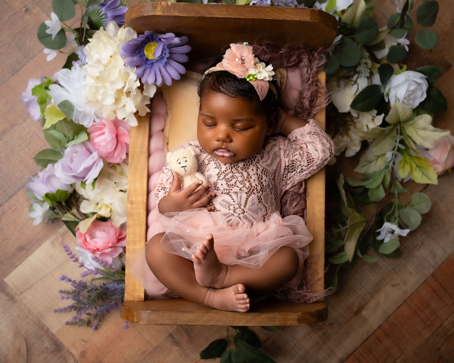 Baby nestled among delicate floral arrangements in soft pink and purple tones.