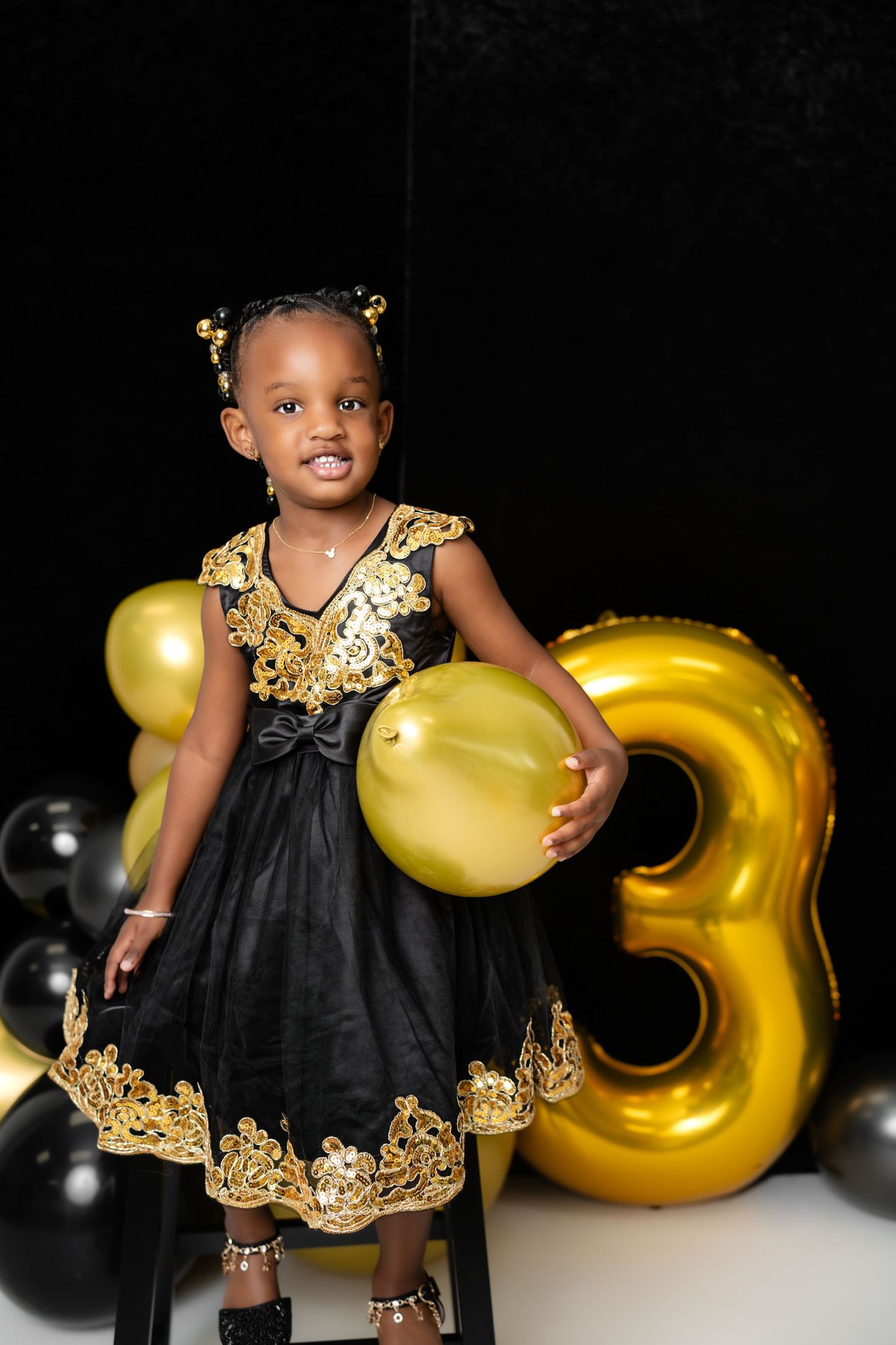 Metro Detroit children photographer Birthday photo shoot with black and gold dress against balloons and dark background.