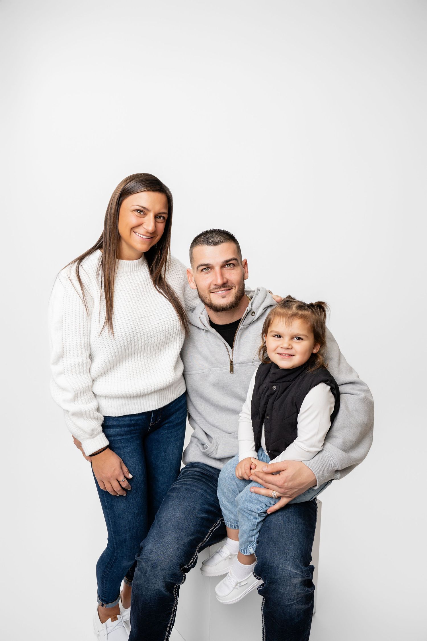 A family in coordinating white and blue outfits poses together against a white background for a casual portrait.