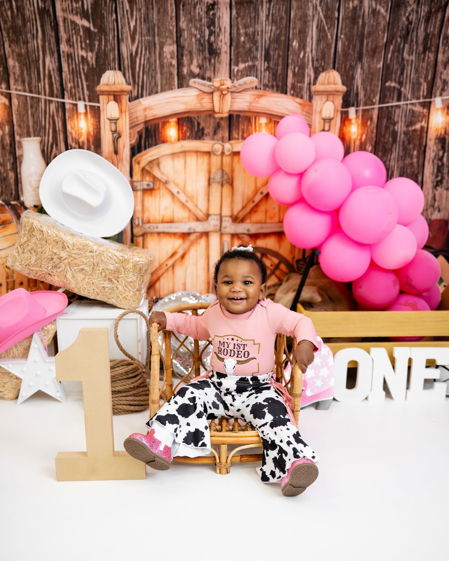 Metro Detroit children photographer photographing a playful toddler in A rustic barn-themed birthday setup with pink balloons,