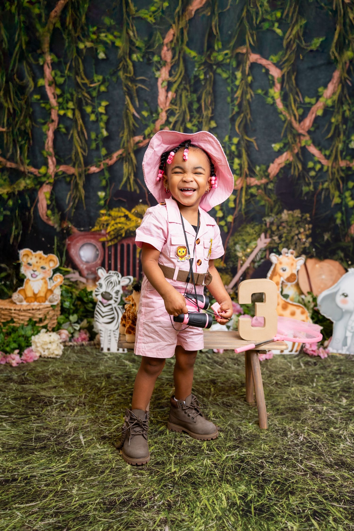 Metro Detroit children photographer photographing a toddle Outdoor safari-themed photo setup with plush animals and hanging vines.