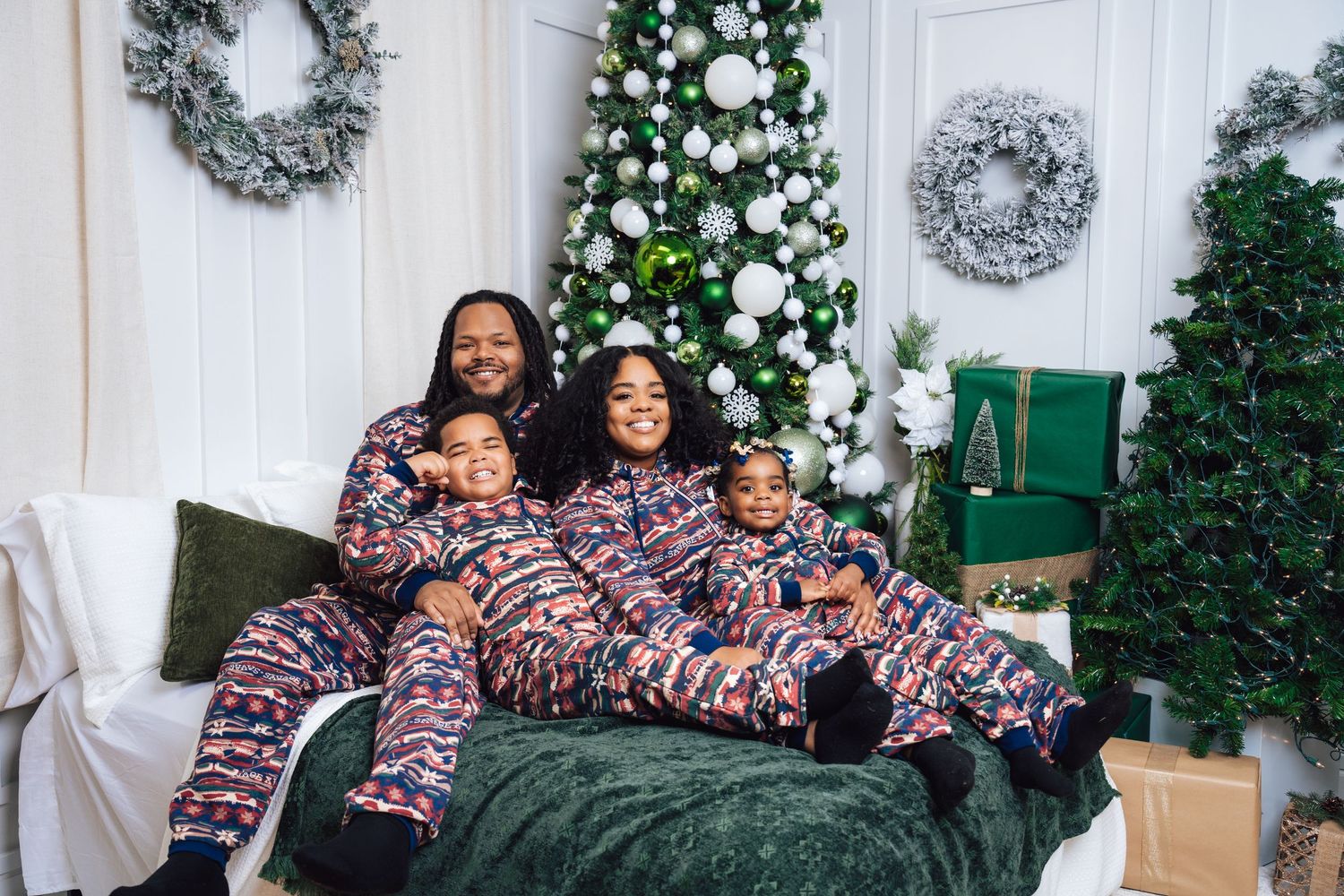 Metro Detroit family photographer capturing  a Family wearing matching Christmas pajamas pose together on white couch with holiday decor.