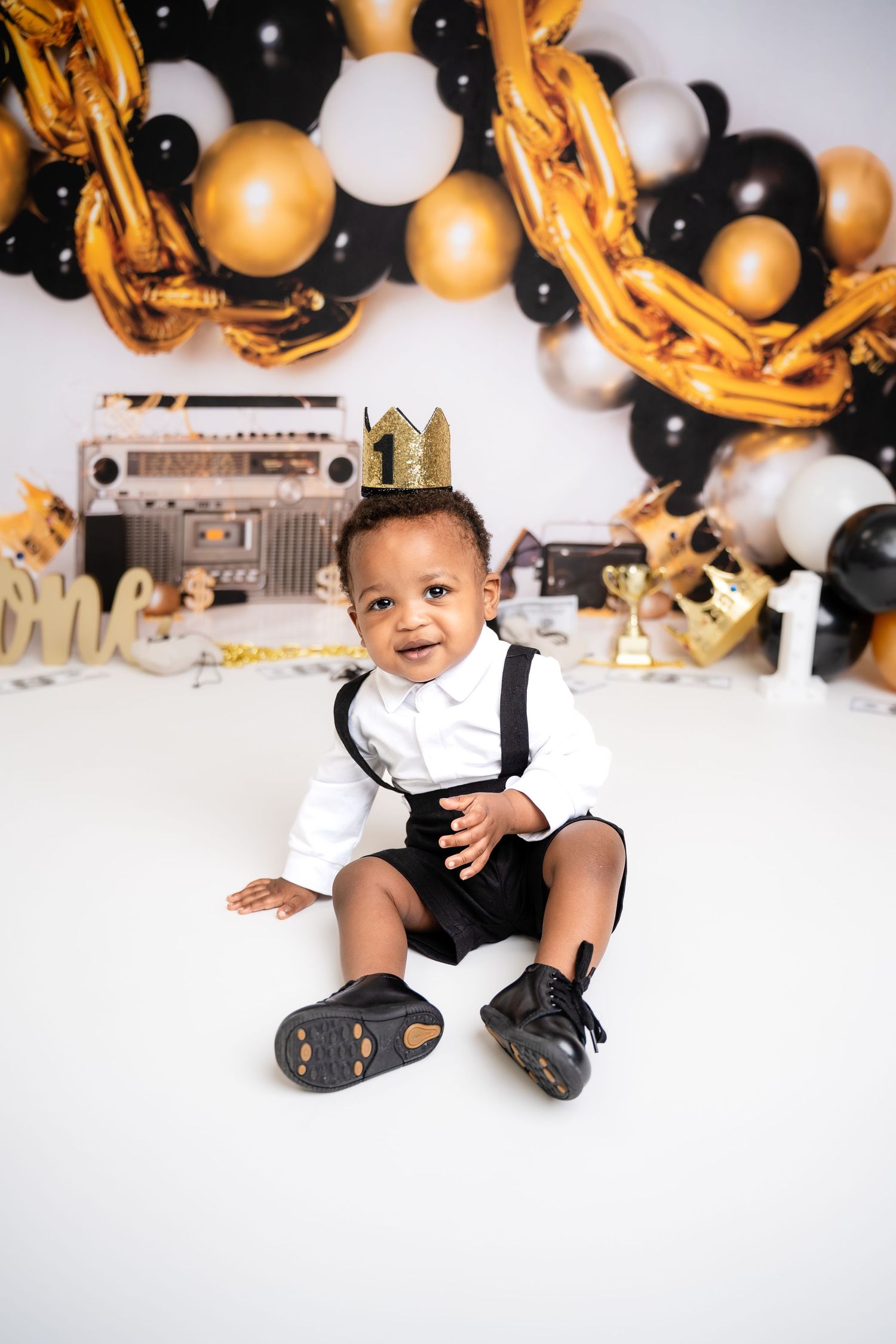 Metro Detroit children photographer Baby photoshoot with gold and black balloons and decorations against white background.