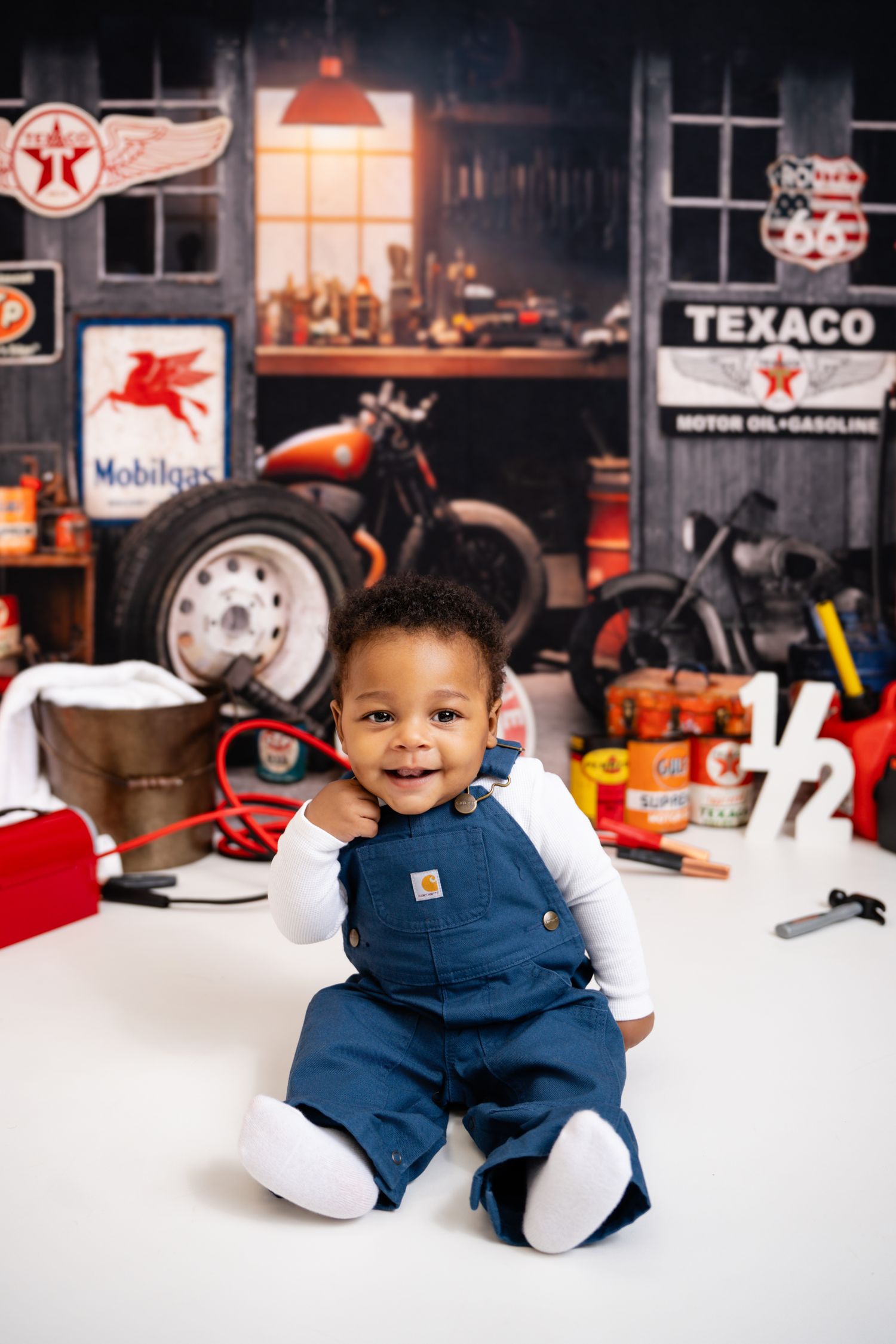 Metro Detroit children photographer photographing a baby in blue overalls sitting and playing in a vintage automotive garage setting.