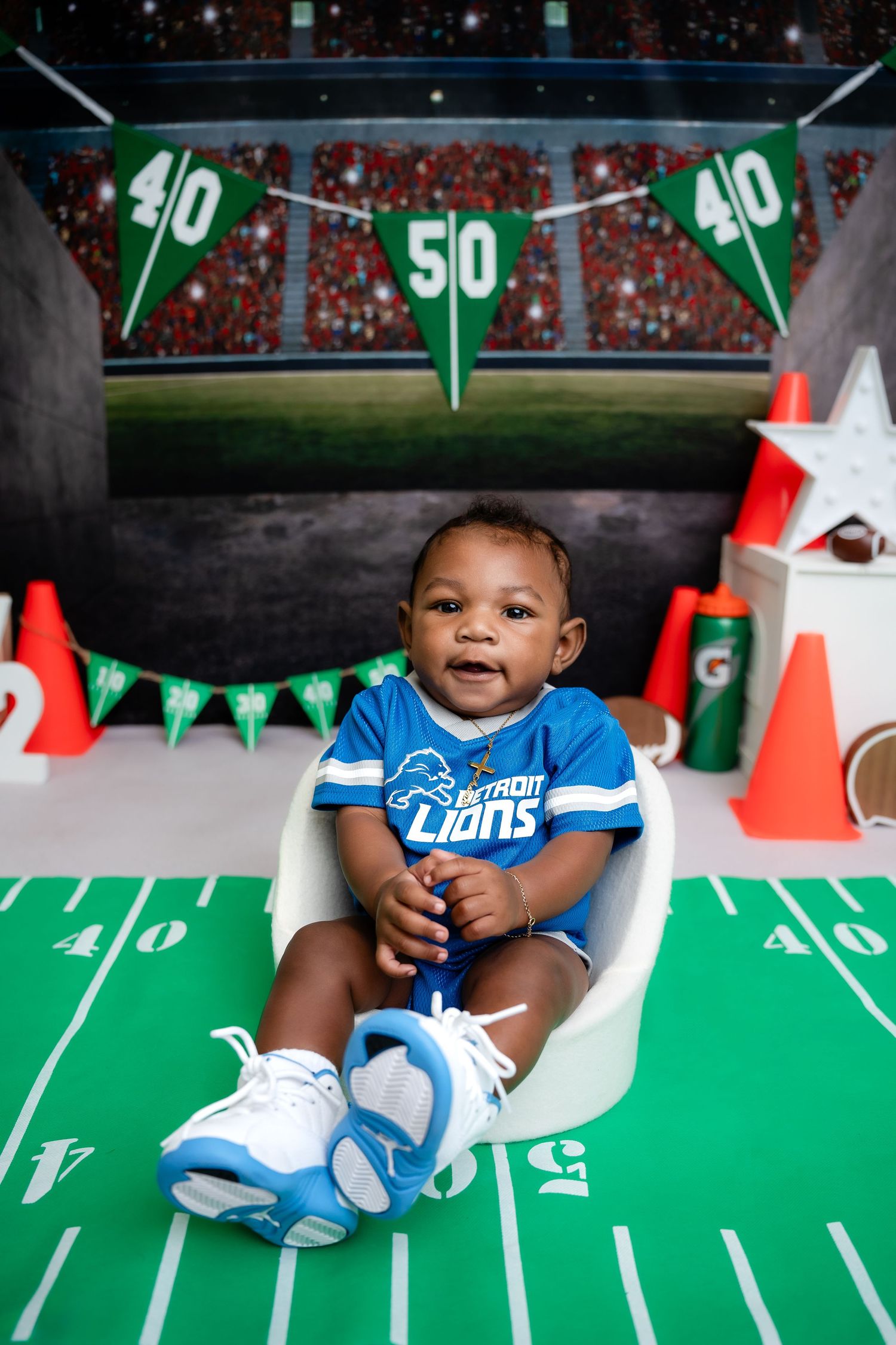 Metro Detroit children photographer capturing a Baby in blue Detroit Lions jersey sits on football field themed set