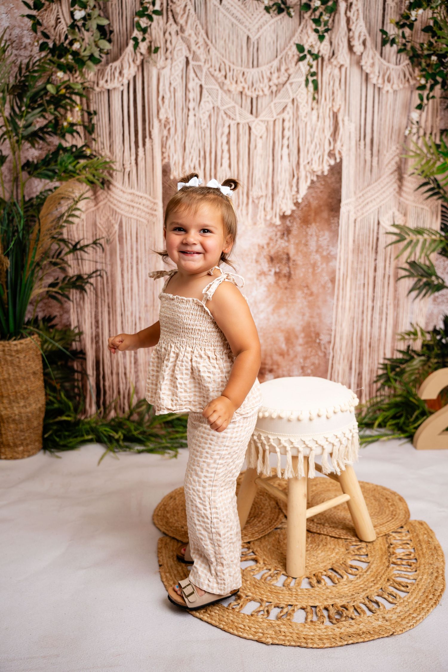 Metro Detroit children A cream-colored macrame backdrop sets the scene for a rustic photo shoot with a decorative wooden stool and jute rug.