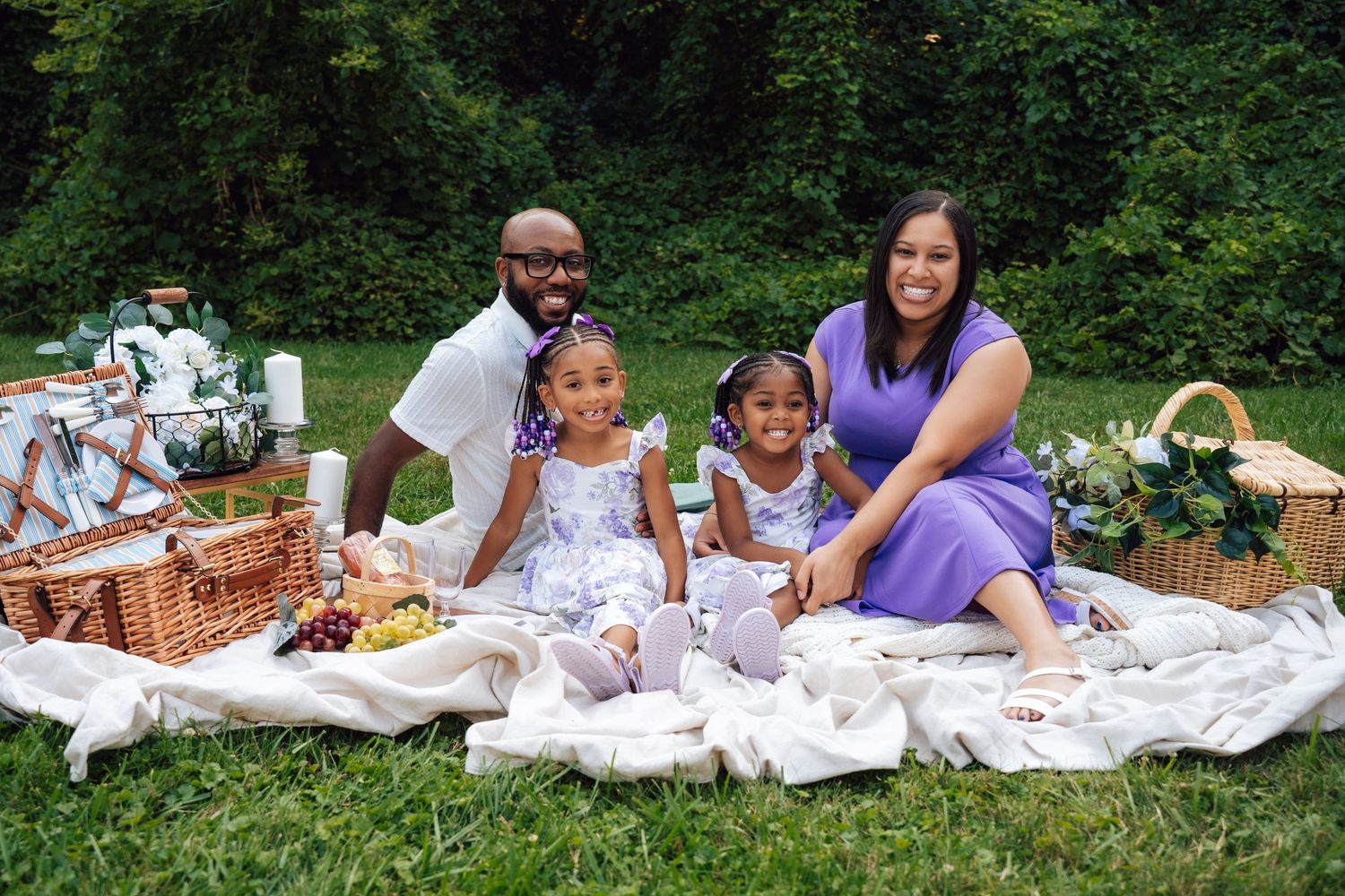 Metro Detroit family photographer capturing Picnic scene with family relaxing on white blanket in park setting with trees in background.